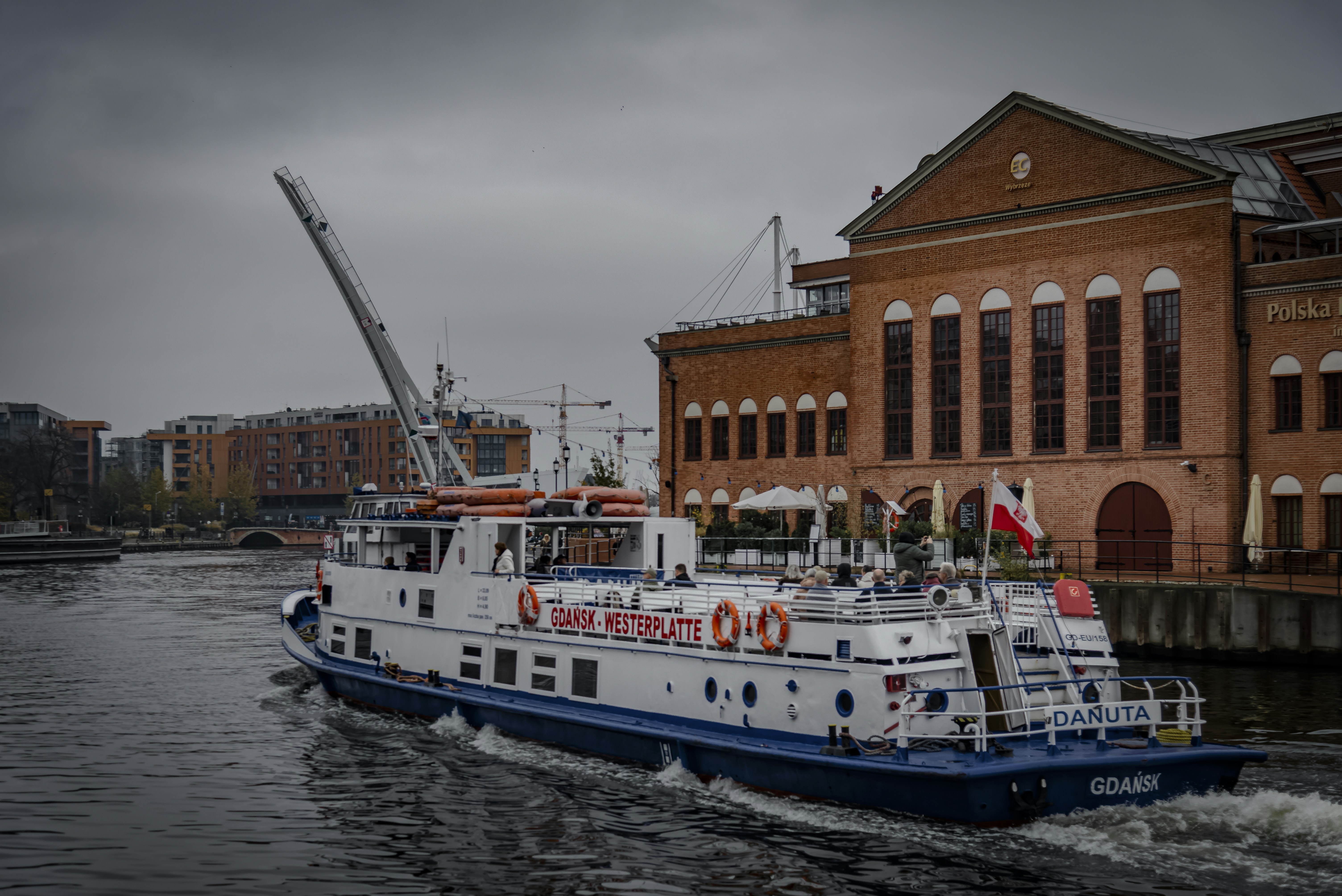A white boat cruises down a canal by buildings.