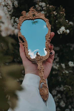 Hand holding ornate vintage mirror reflecting sky