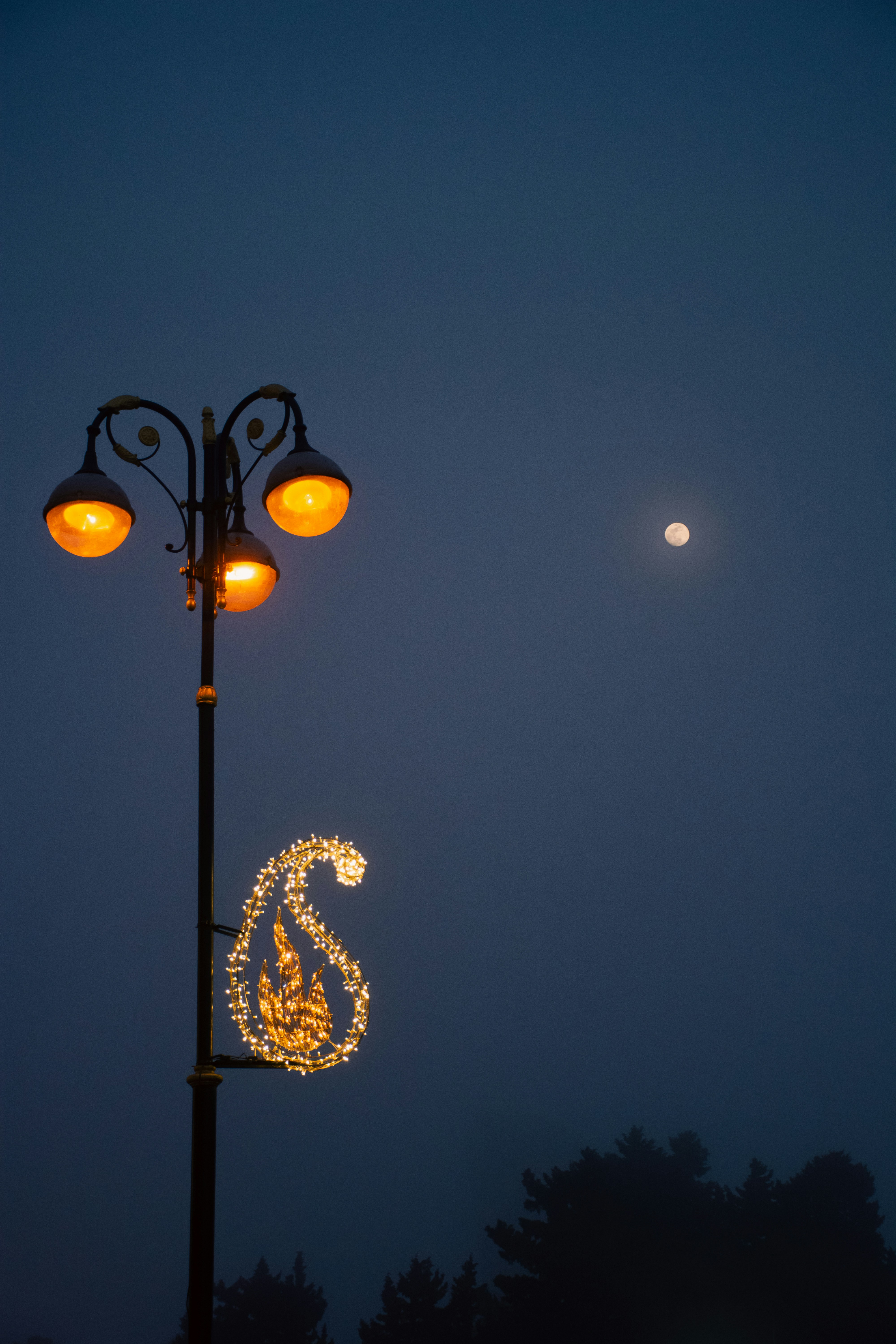 Street lamp with paisley decoration and moon in fog.
