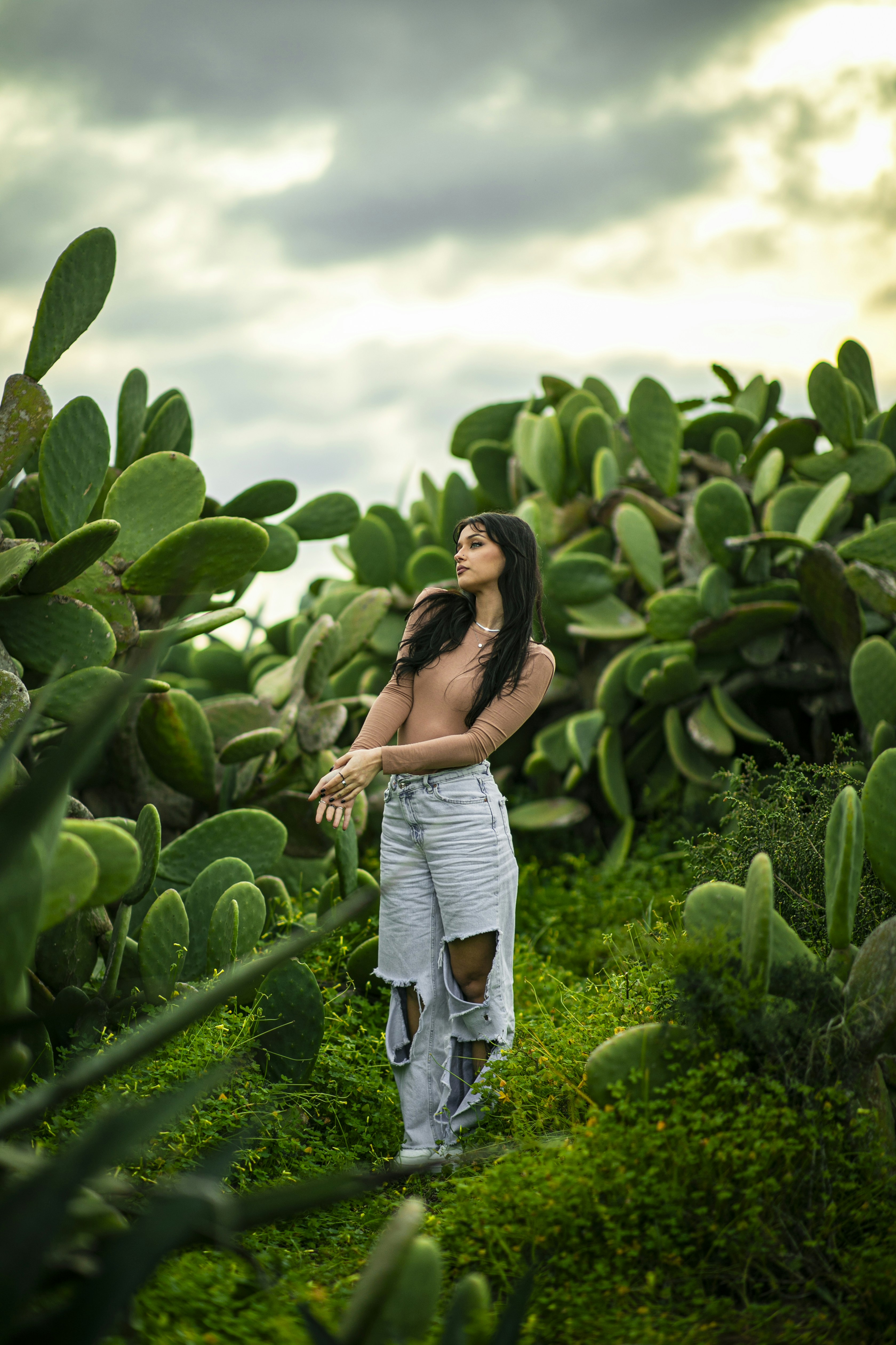 Woman standing amidst lush green cacti under a cloudy sky