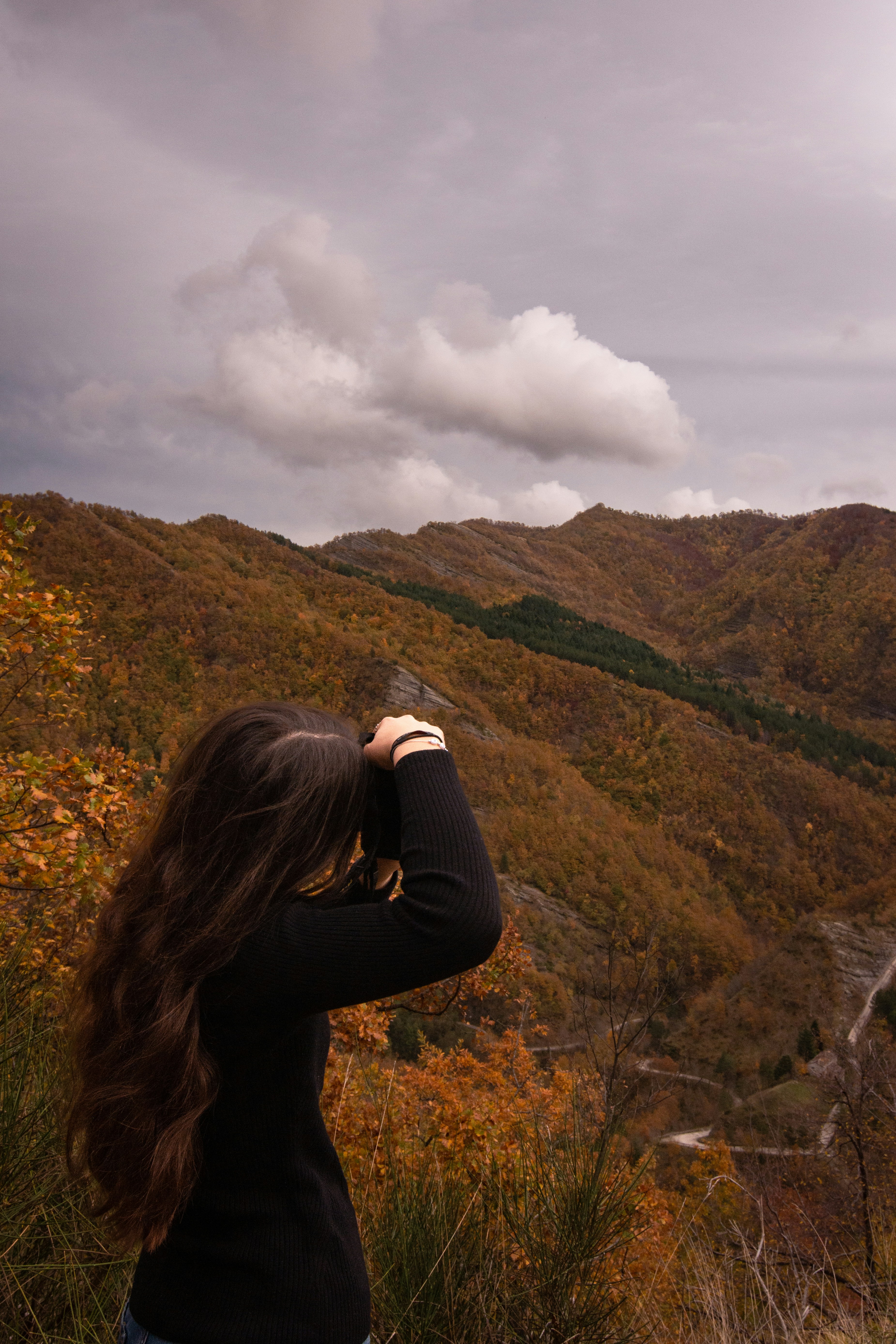 Woman looking through binoculars at autumn mountains.