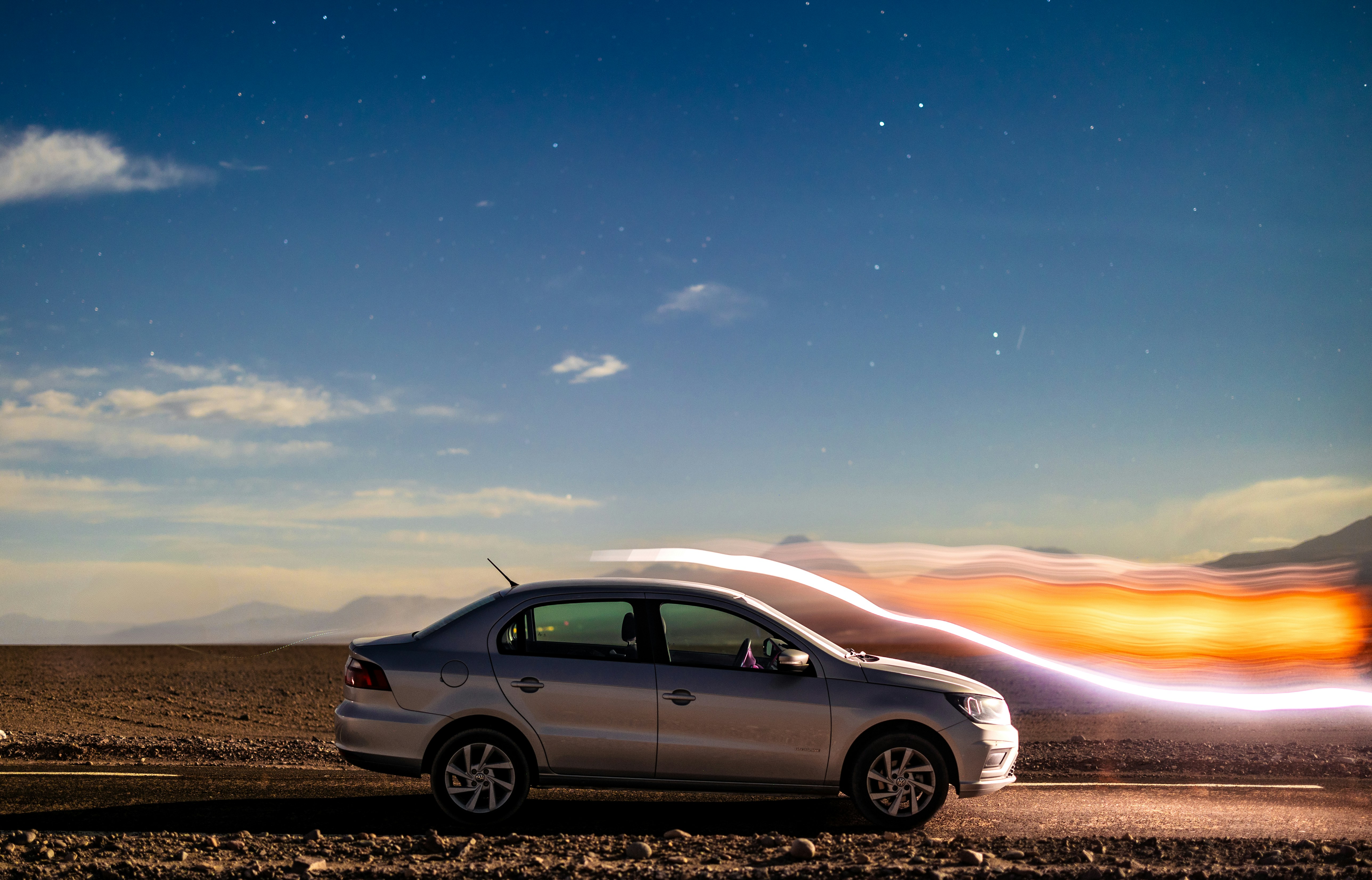 Silver sedan driving on a desert road at night.
