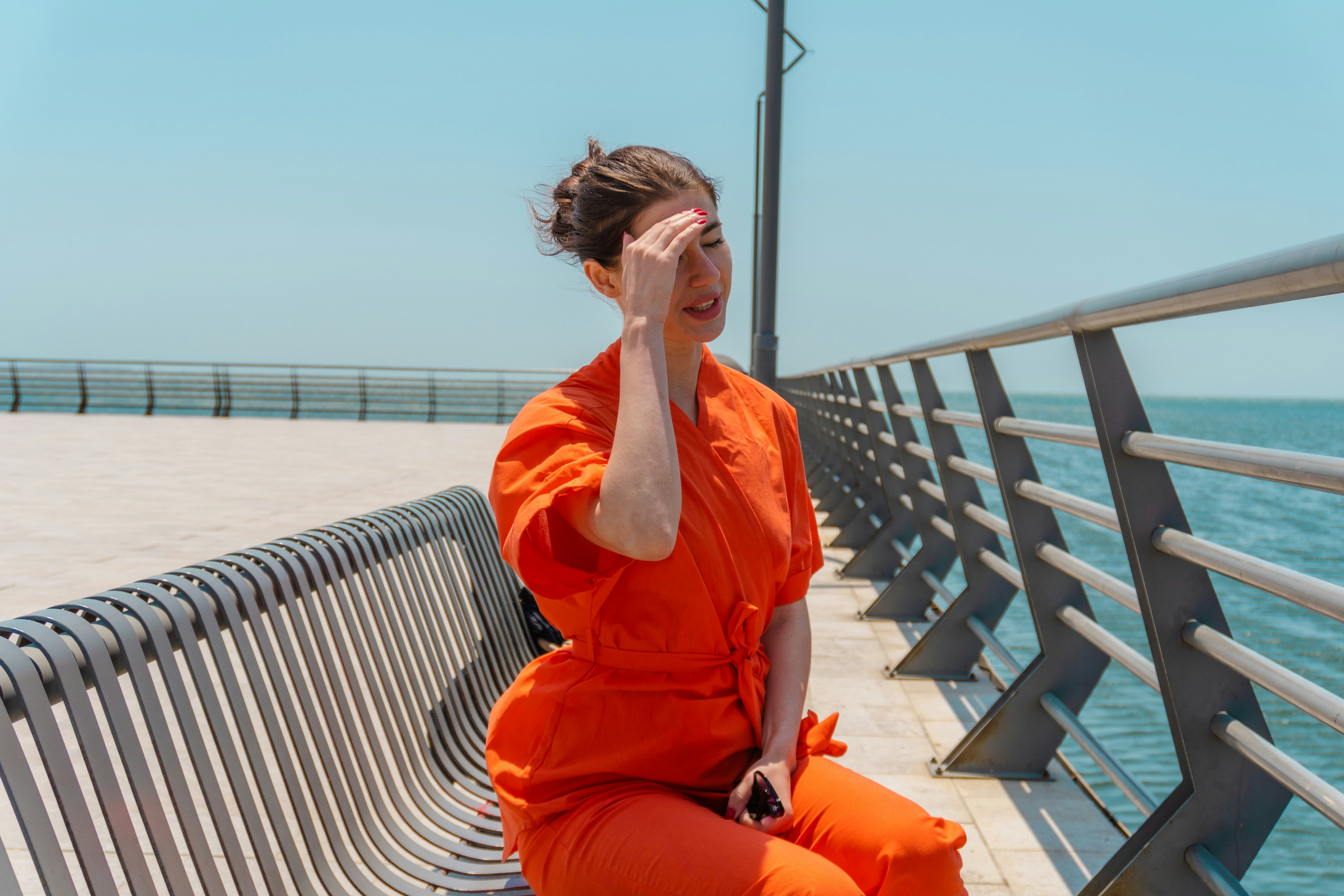 Woman in orange jumpsuit sits by the water. (Photo by Zulfugar Karimov on Unsplash)