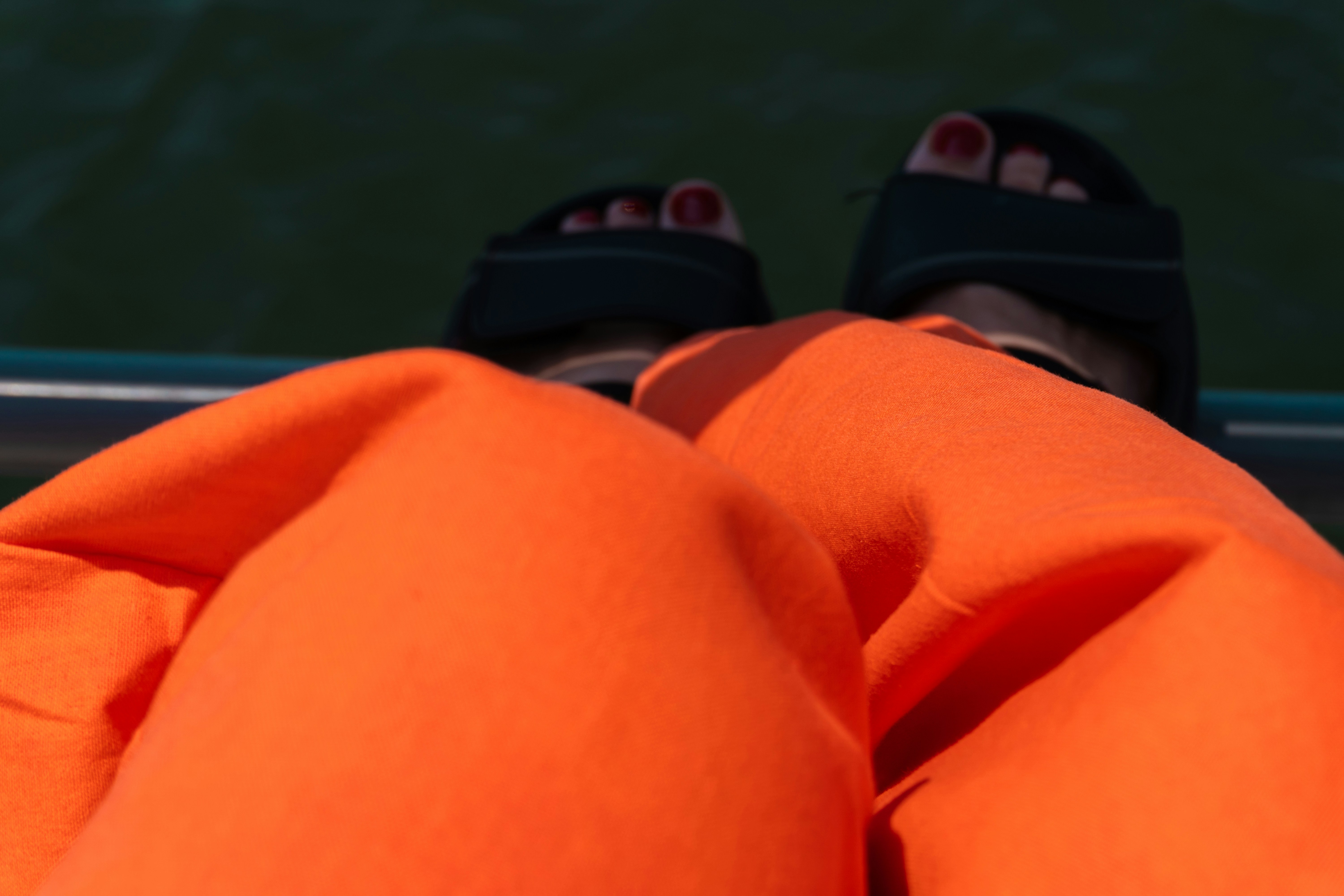 Person's legs in orange pants and sandals by water.