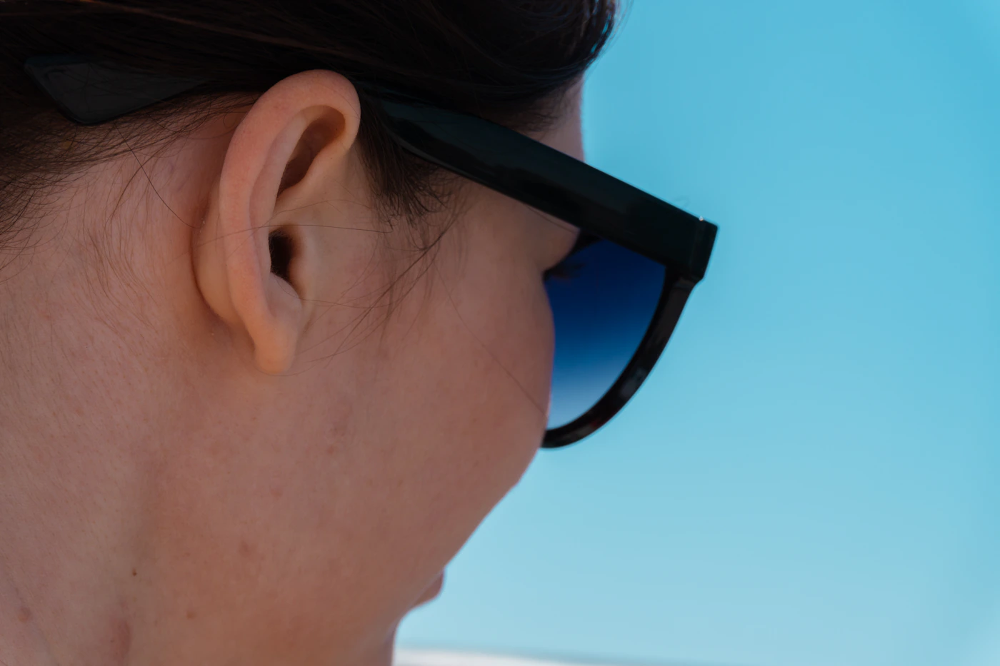 Woman wearing sculpted black sunglasses against a bright blue sky