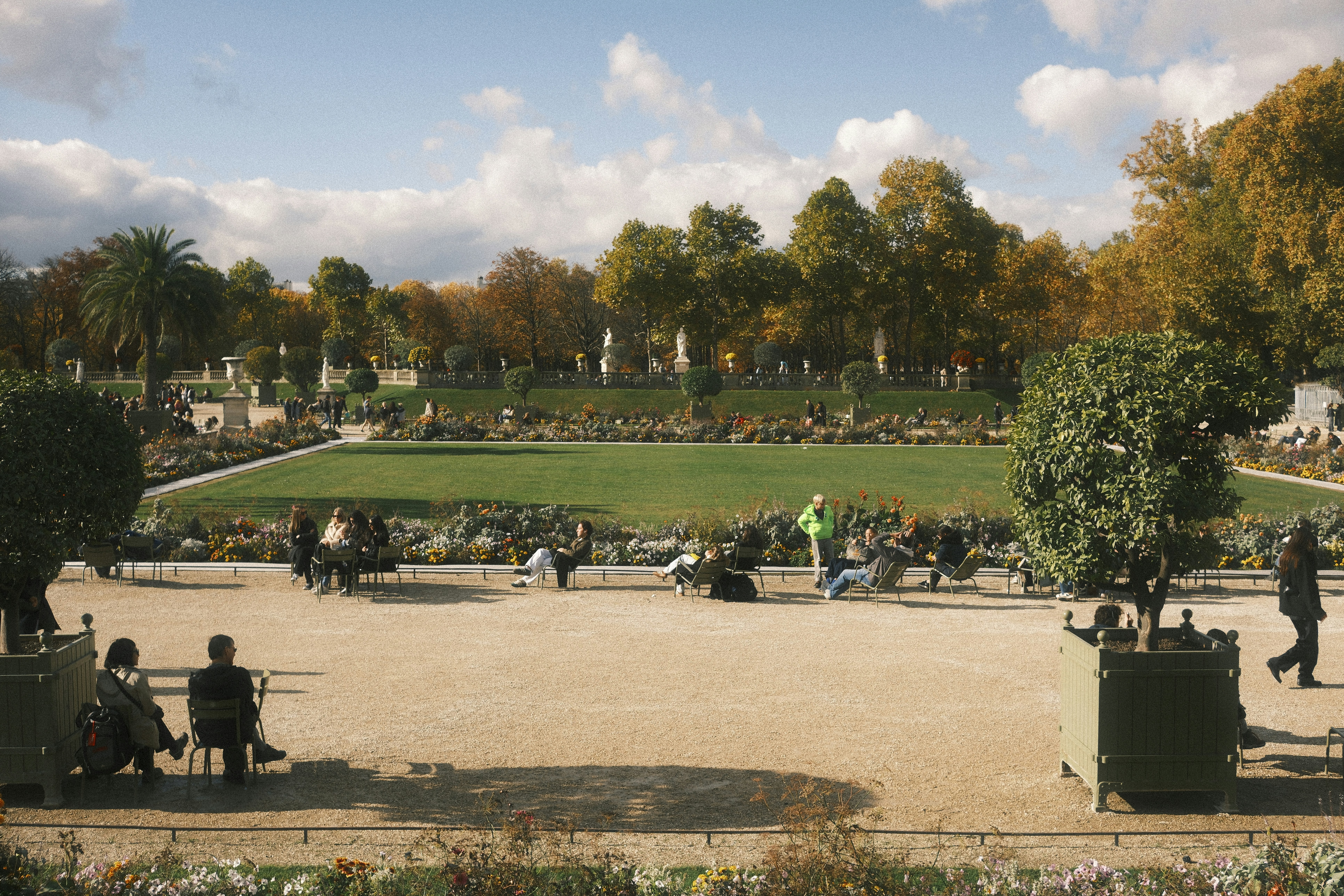 People relaxing in a park with autumn trees and statues.