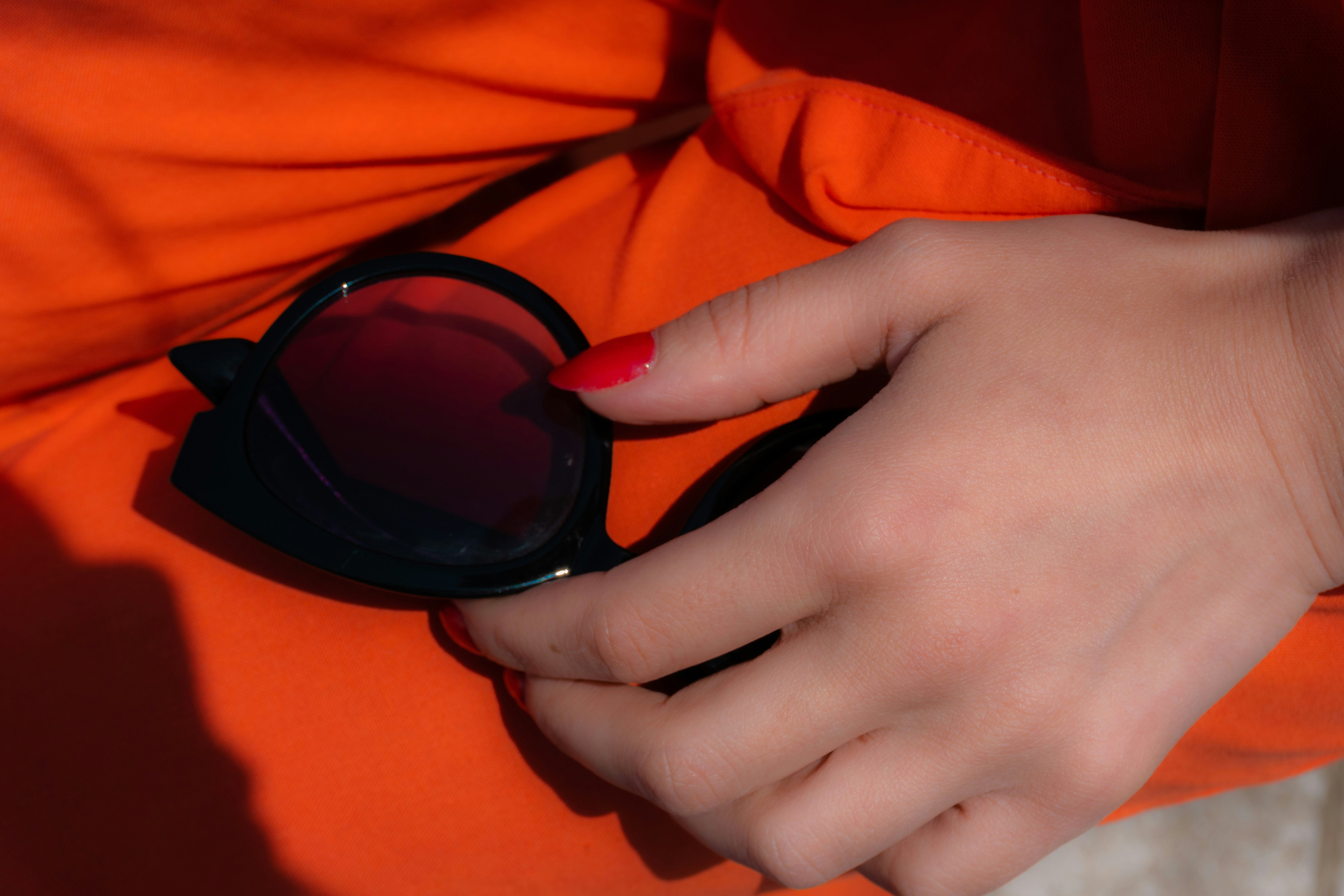 Main de femme tenant des lunettes de soleil noires avec des verres rouges.