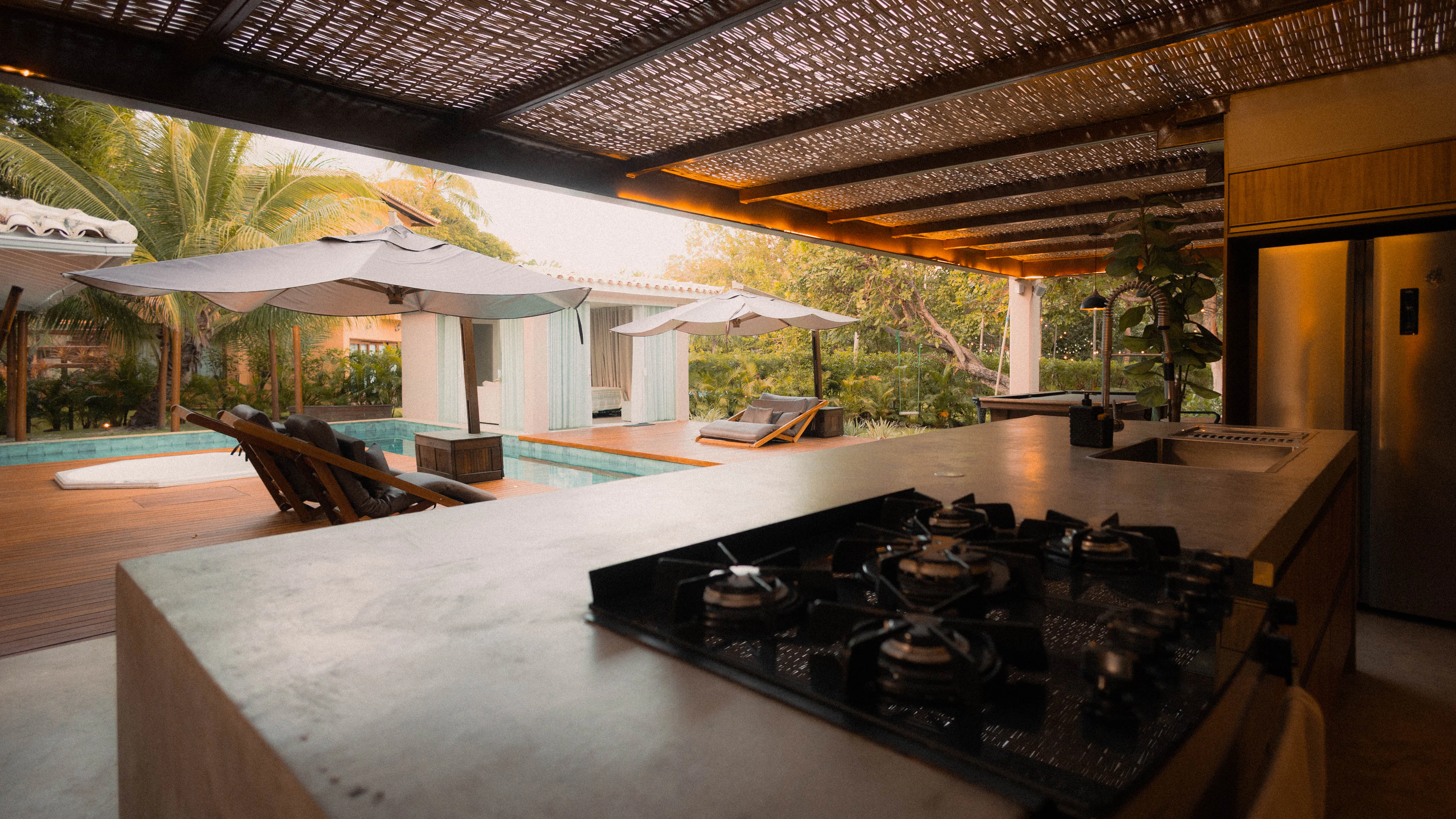 Covered outdoor kitchen with a stone counter looking out over a pool