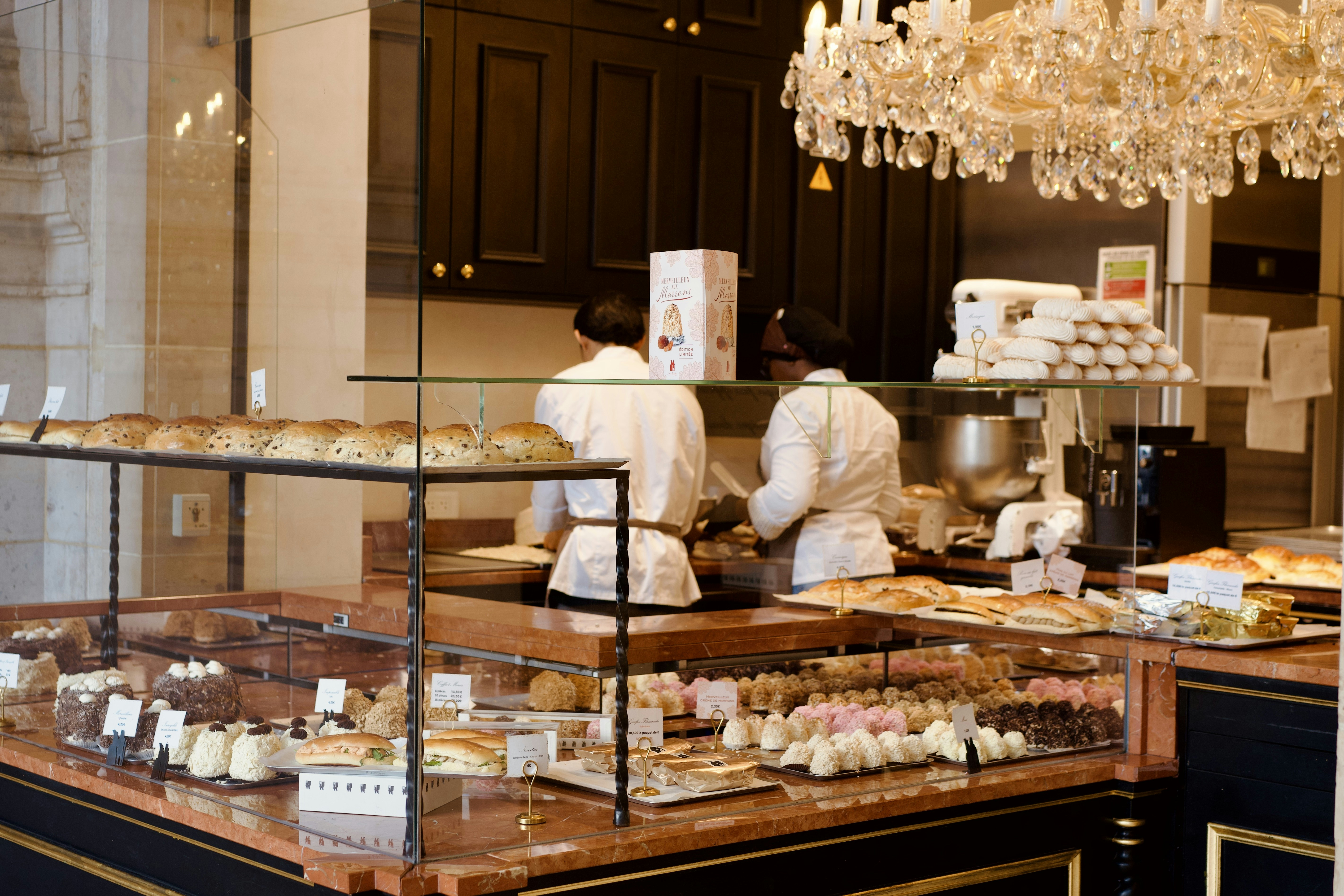 Pastry display case with chefs preparing food in background.