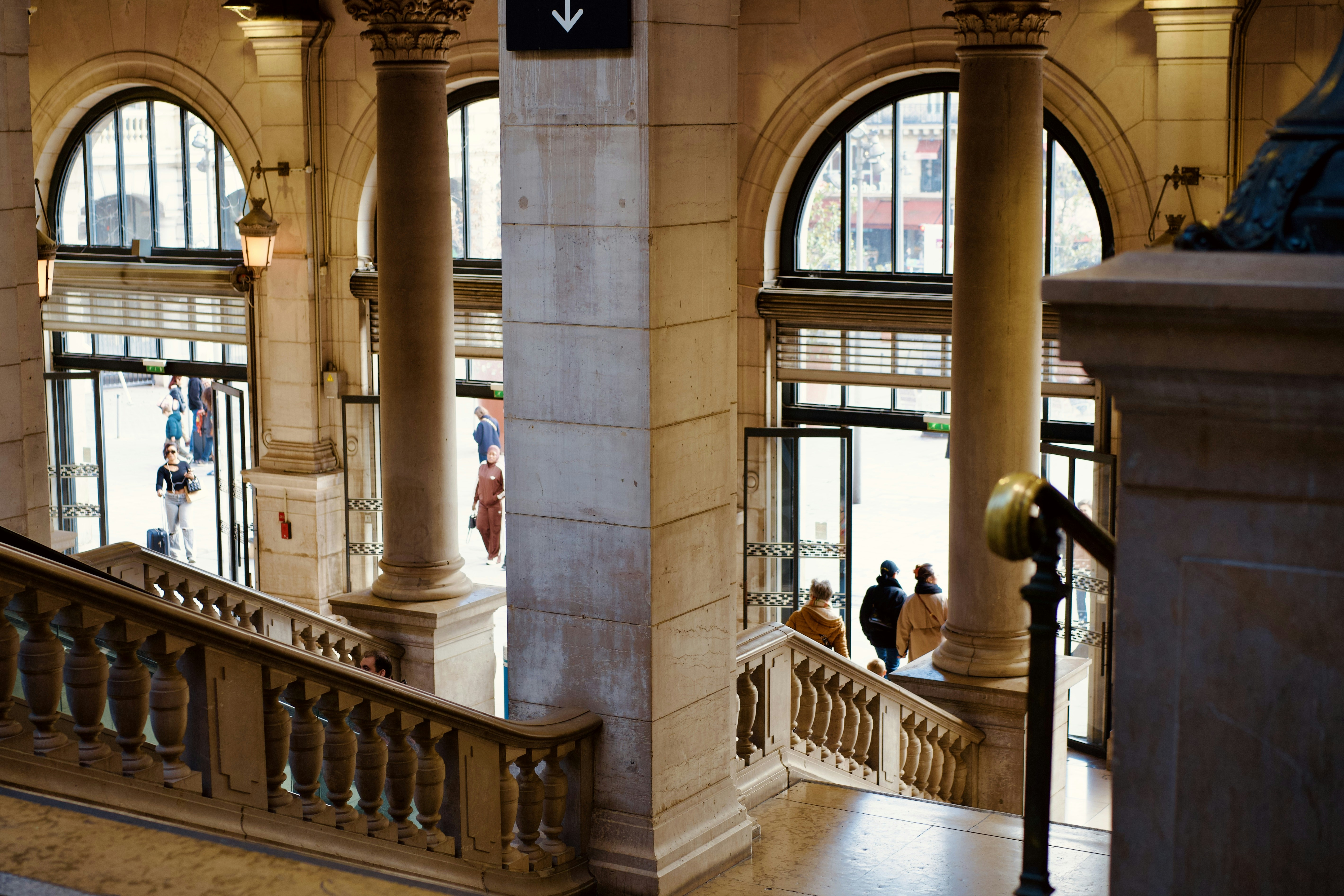 People walking up grand marble staircase with arched windows.