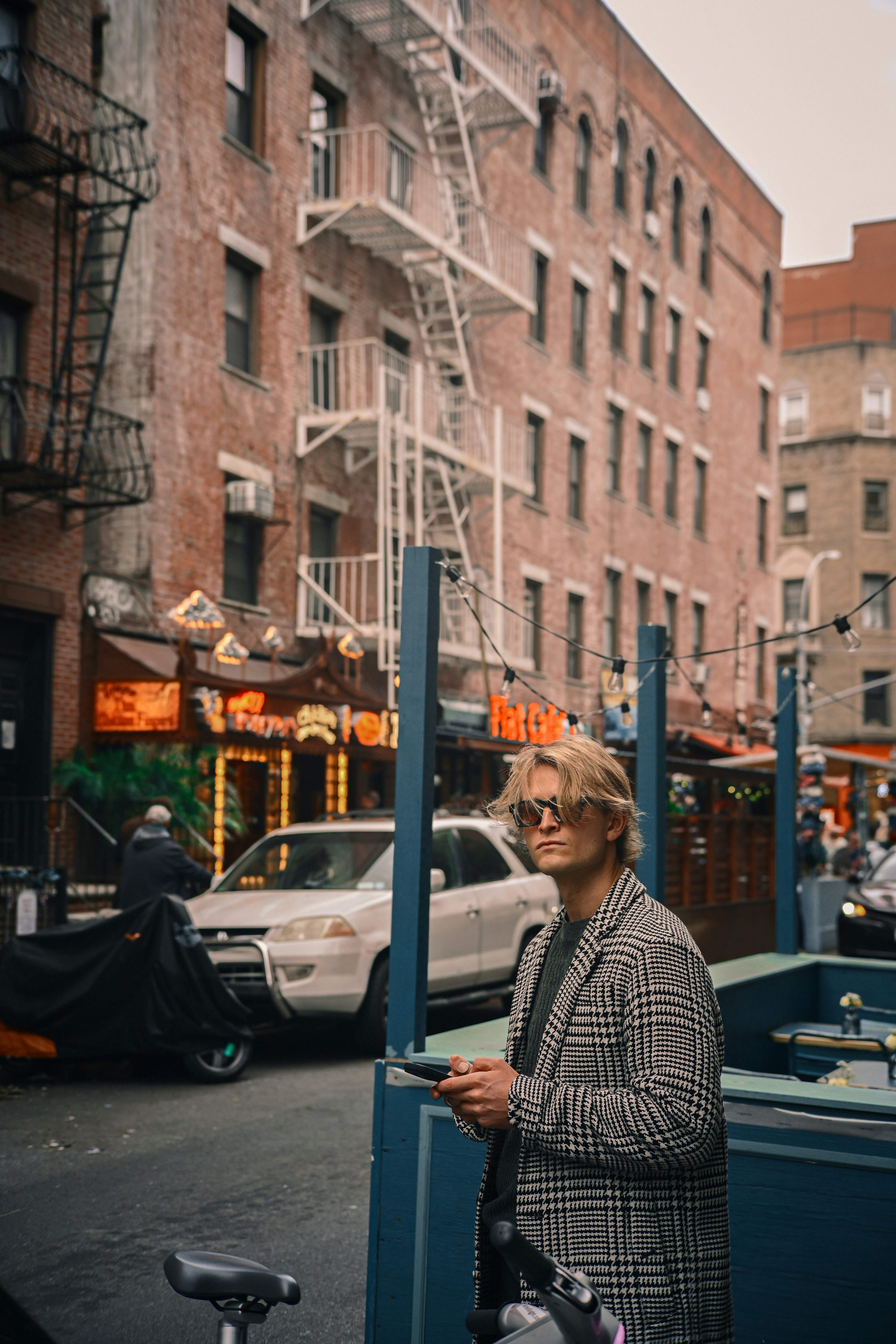 Man in plaid jacket looking at phone on city street