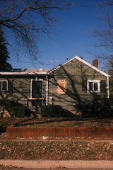 A weathered green house with boarded window.