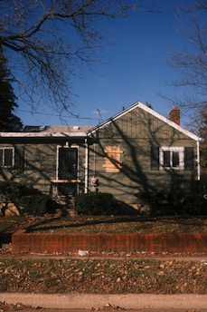 A weathered green house with boarded window.