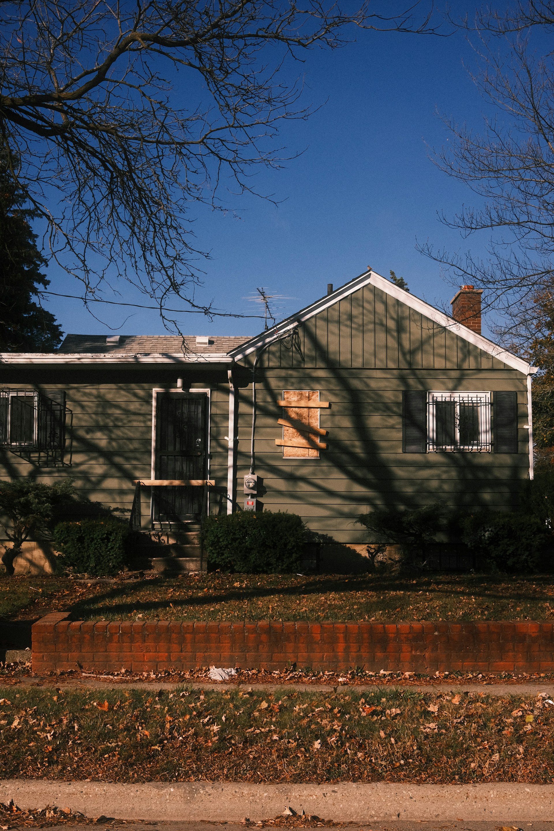 A weathered green house with boarded window.