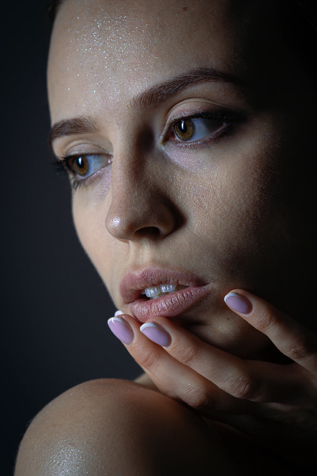 Rostro de una mujer con la mano junto a los labios, sobre fondo oscuro