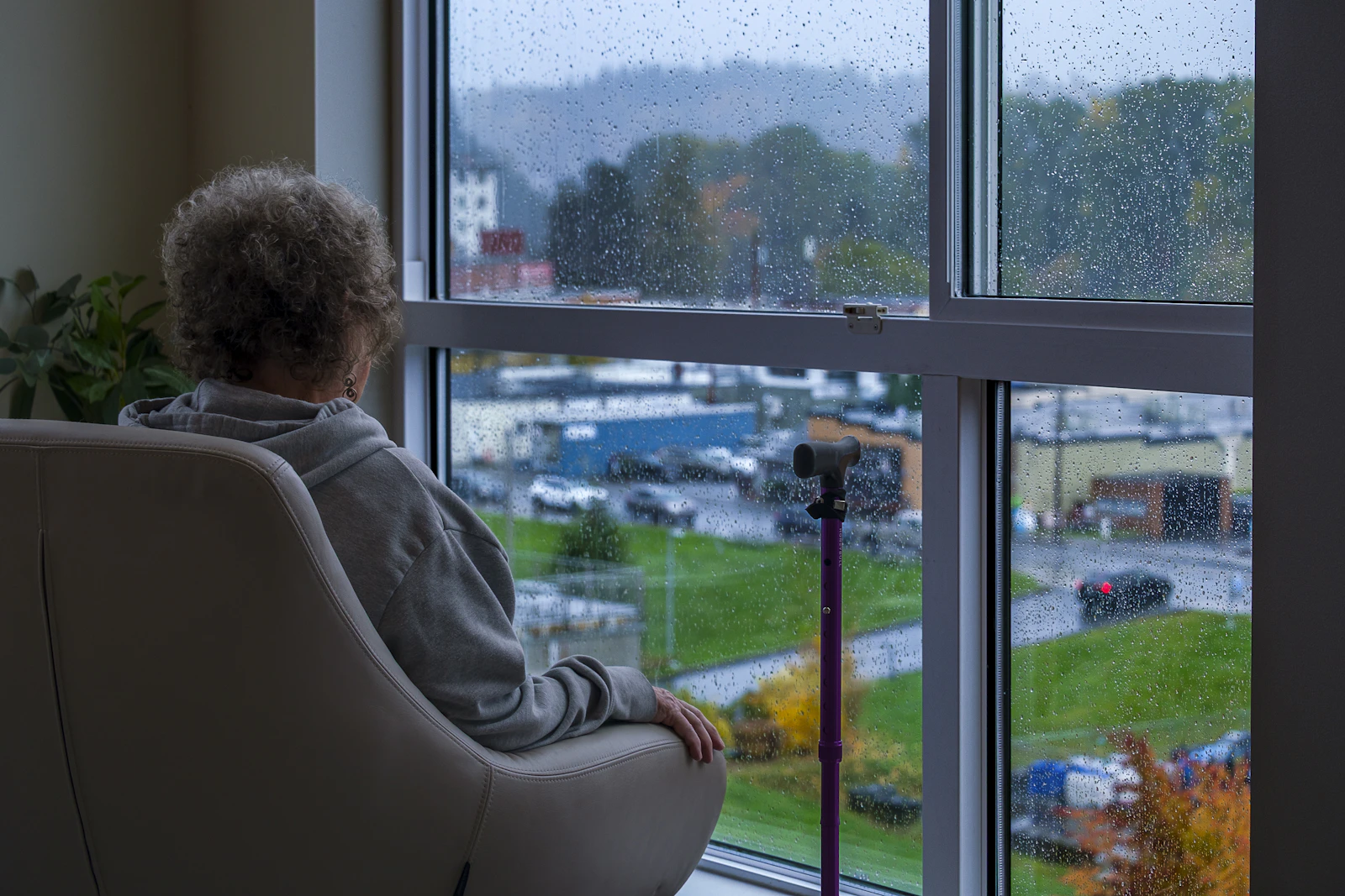 A woman sitting in an armchair looking out a rainy window, thinking quietly