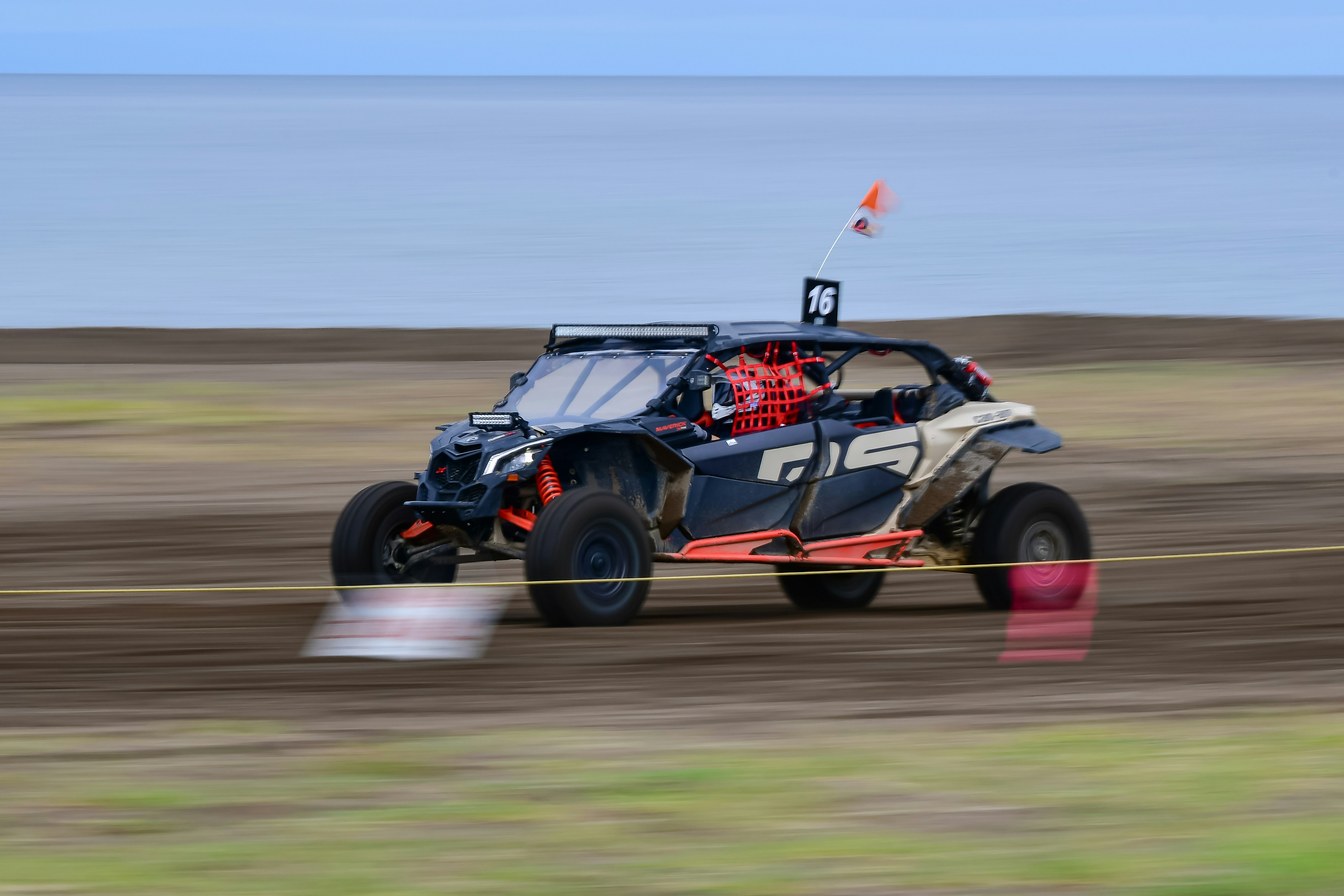 A side-by-side off-road vehicle racing on a dirt track.