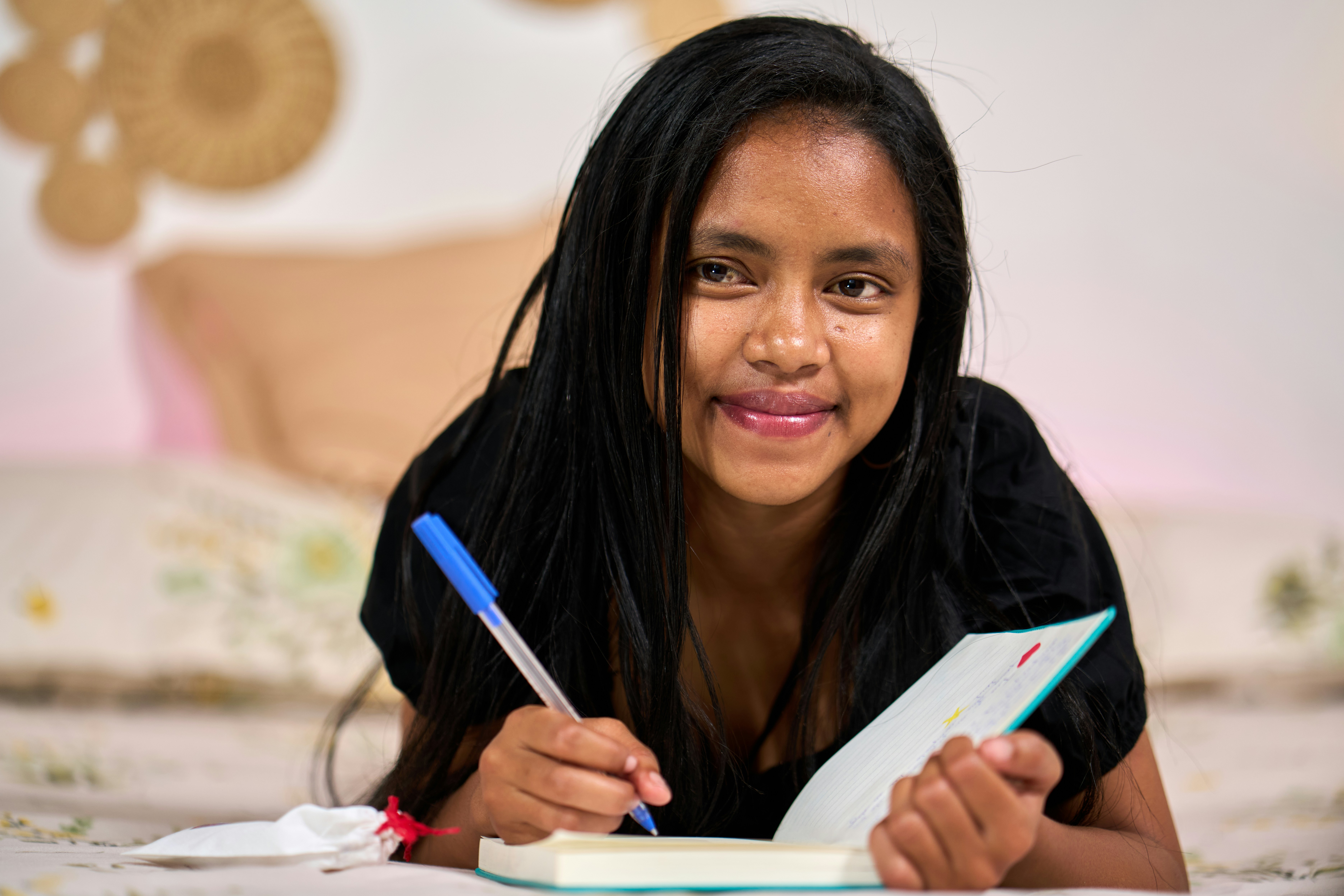 Mujer joven acostada escribiendo en cuaderno