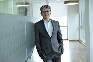 A man in a suit stands in an office hallway.