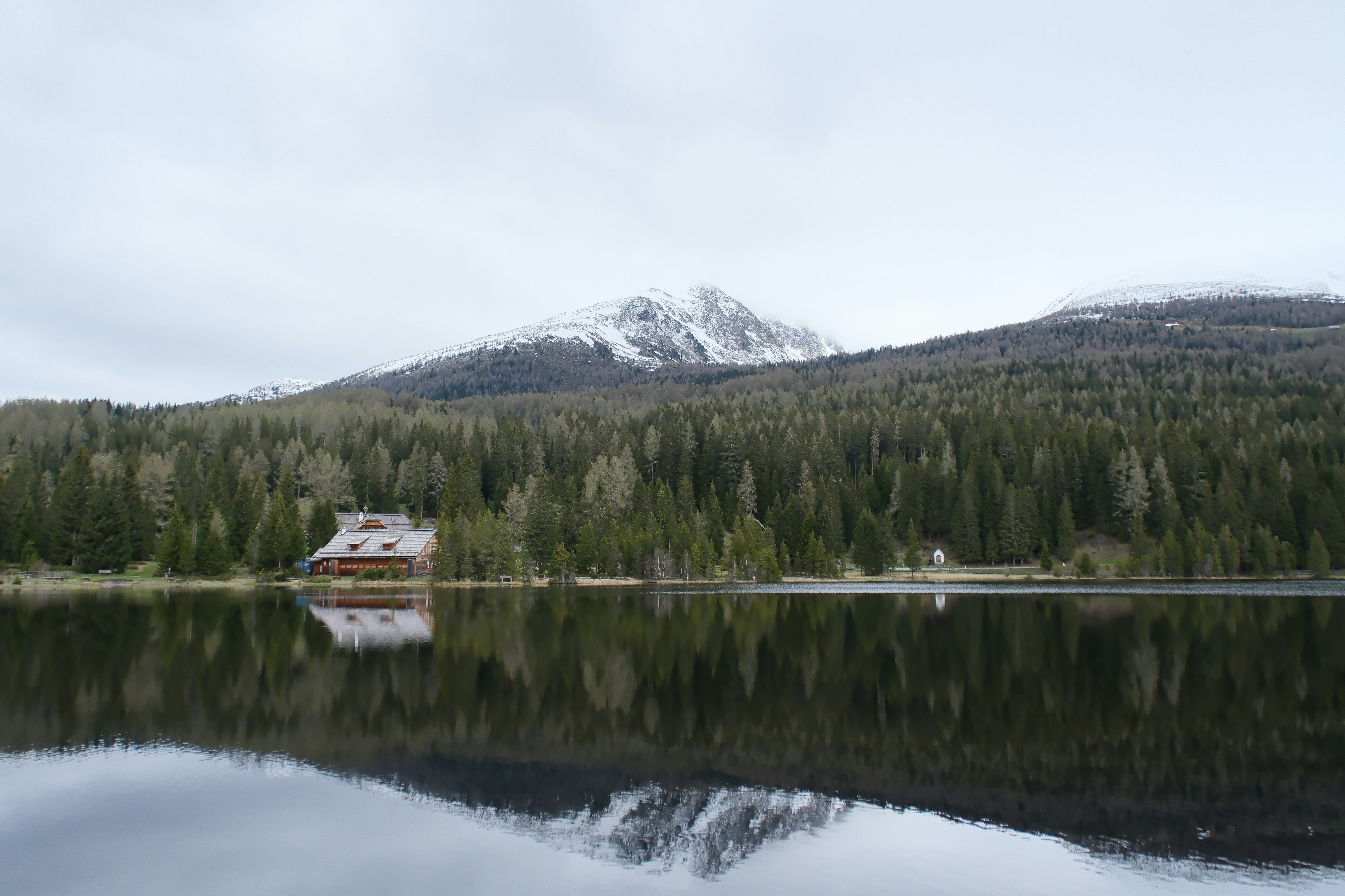 Log cabin by a lake with snow-capped mountains.