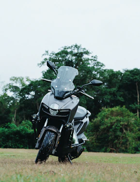 A dark grey scooter parked on grassy field.