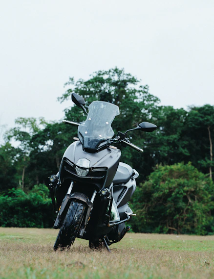 A dark grey scooter parked on grassy field.