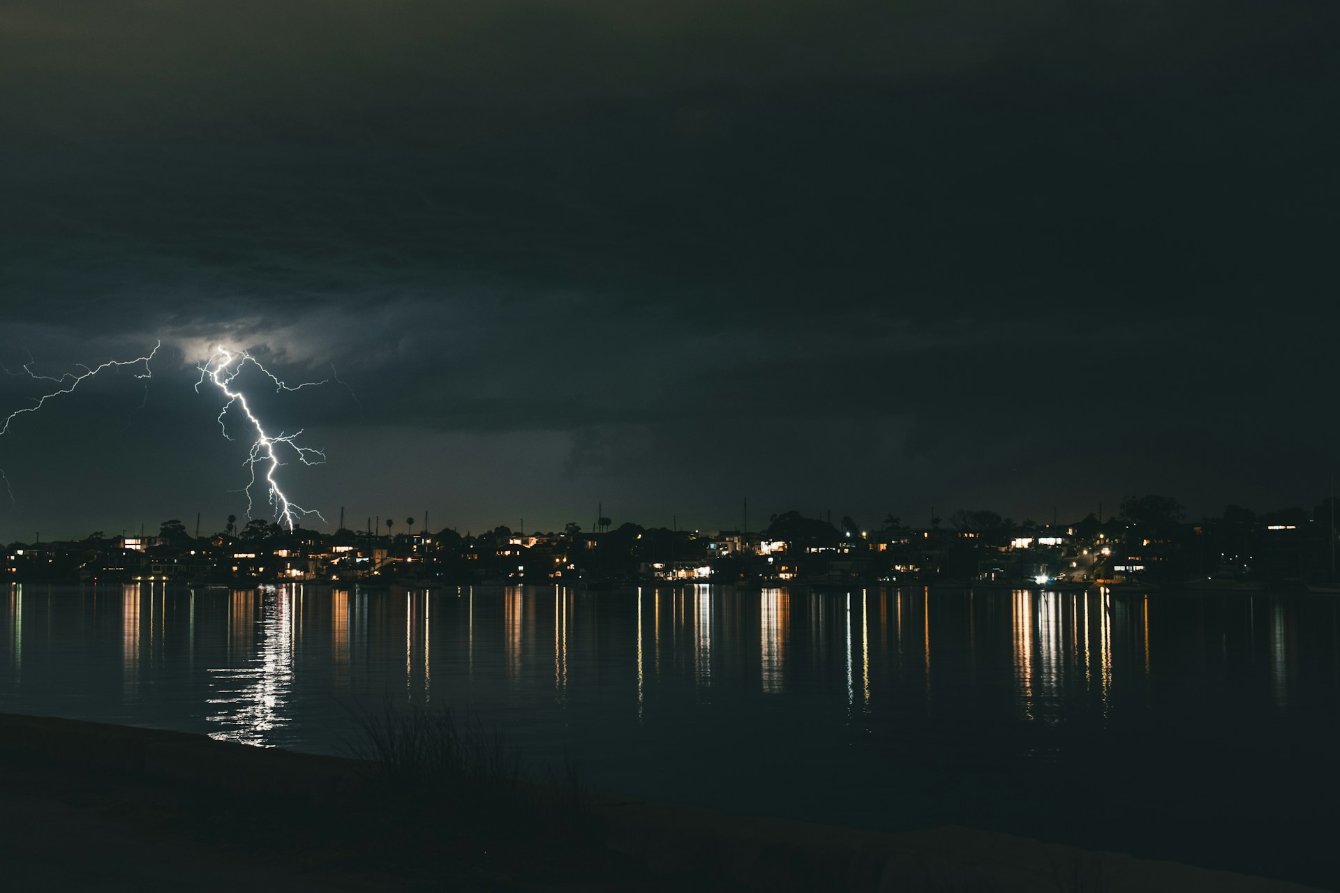 Lightning strikes over a city skyline reflected in water
