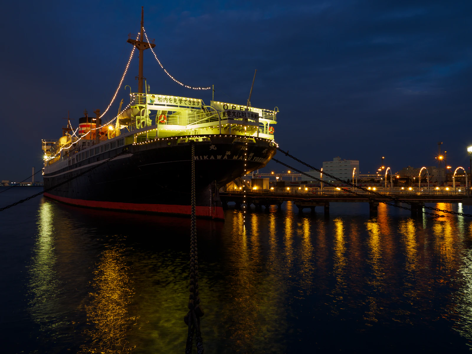 Large cruise ship lit up at night, its lights reflecting on the water