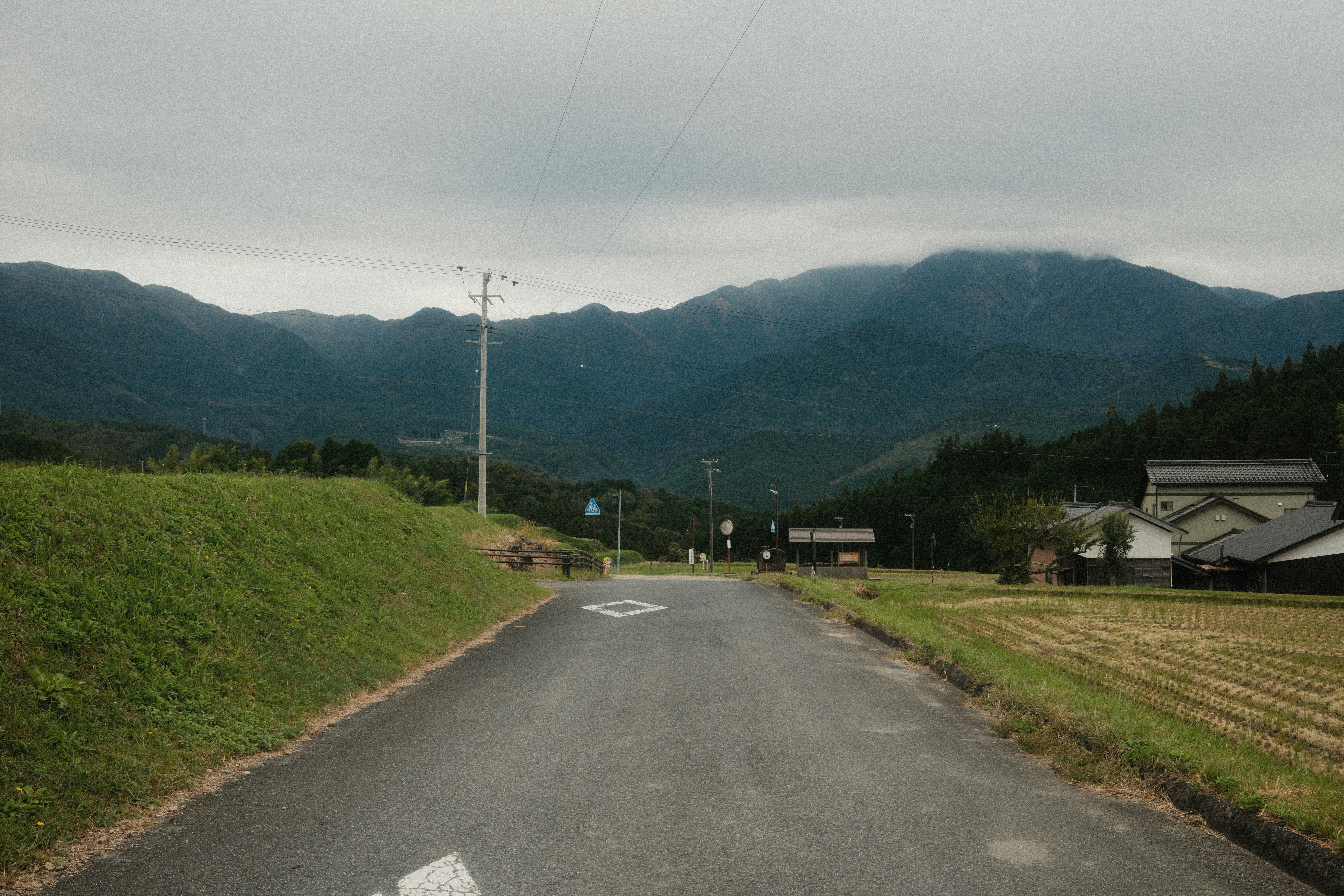 Rural road leading to misty mountains under cloudy sky