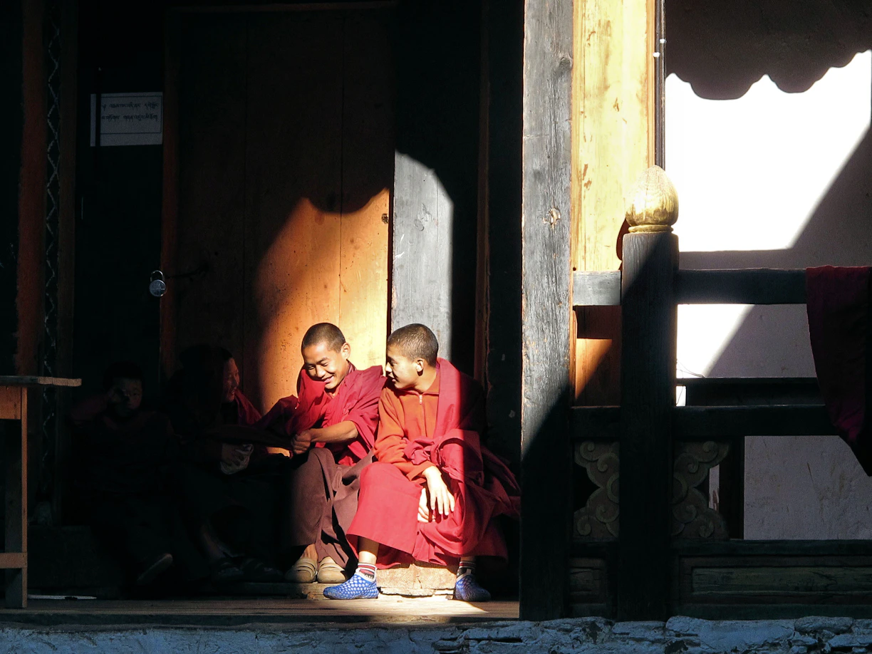 Two young monks in red robes sit in sunlight.