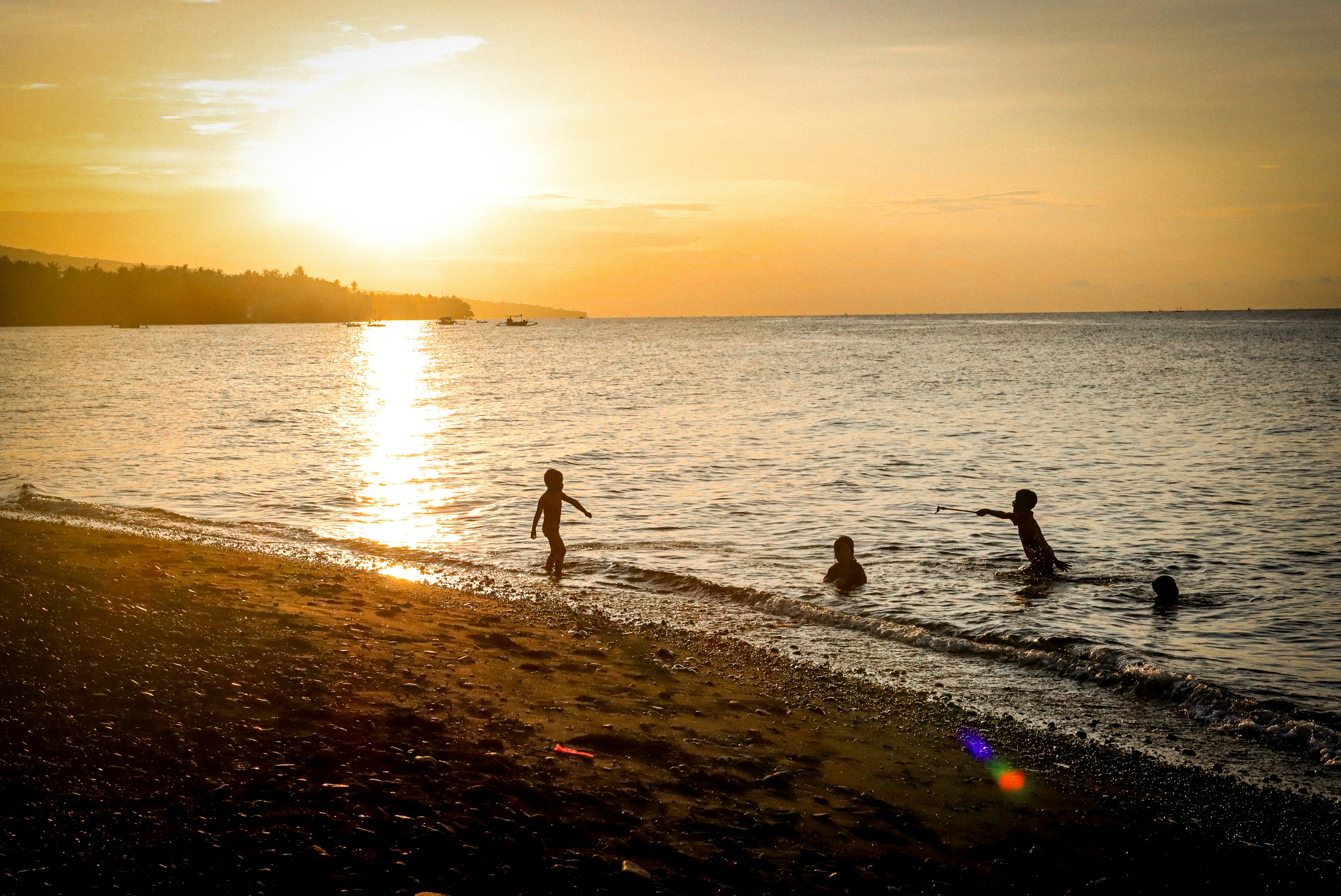 Children playing in the ocean at sunset.