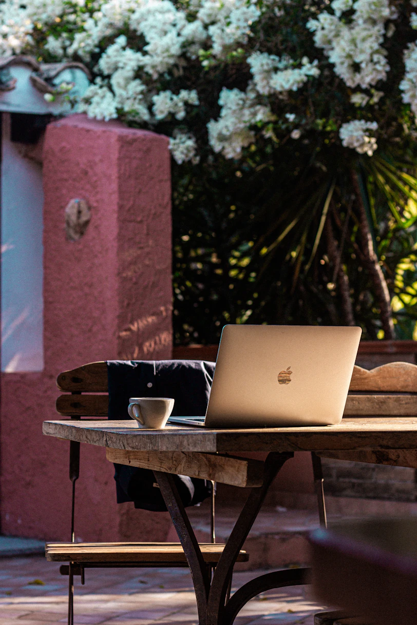 Laptop and coffee cup on a rustic outdoor table.