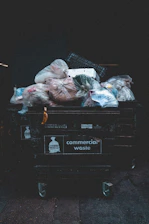 Overflowing commercial waste bin filled with plastic bags.