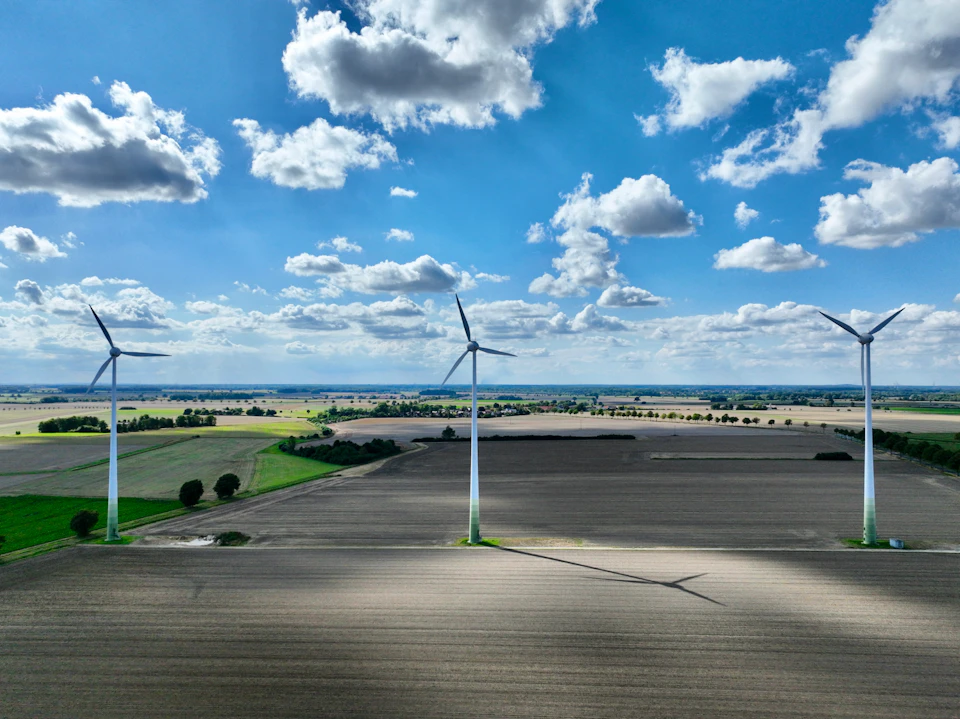 Three large wind turbines stand tall in a rural landscape amidst fluffy white clouds