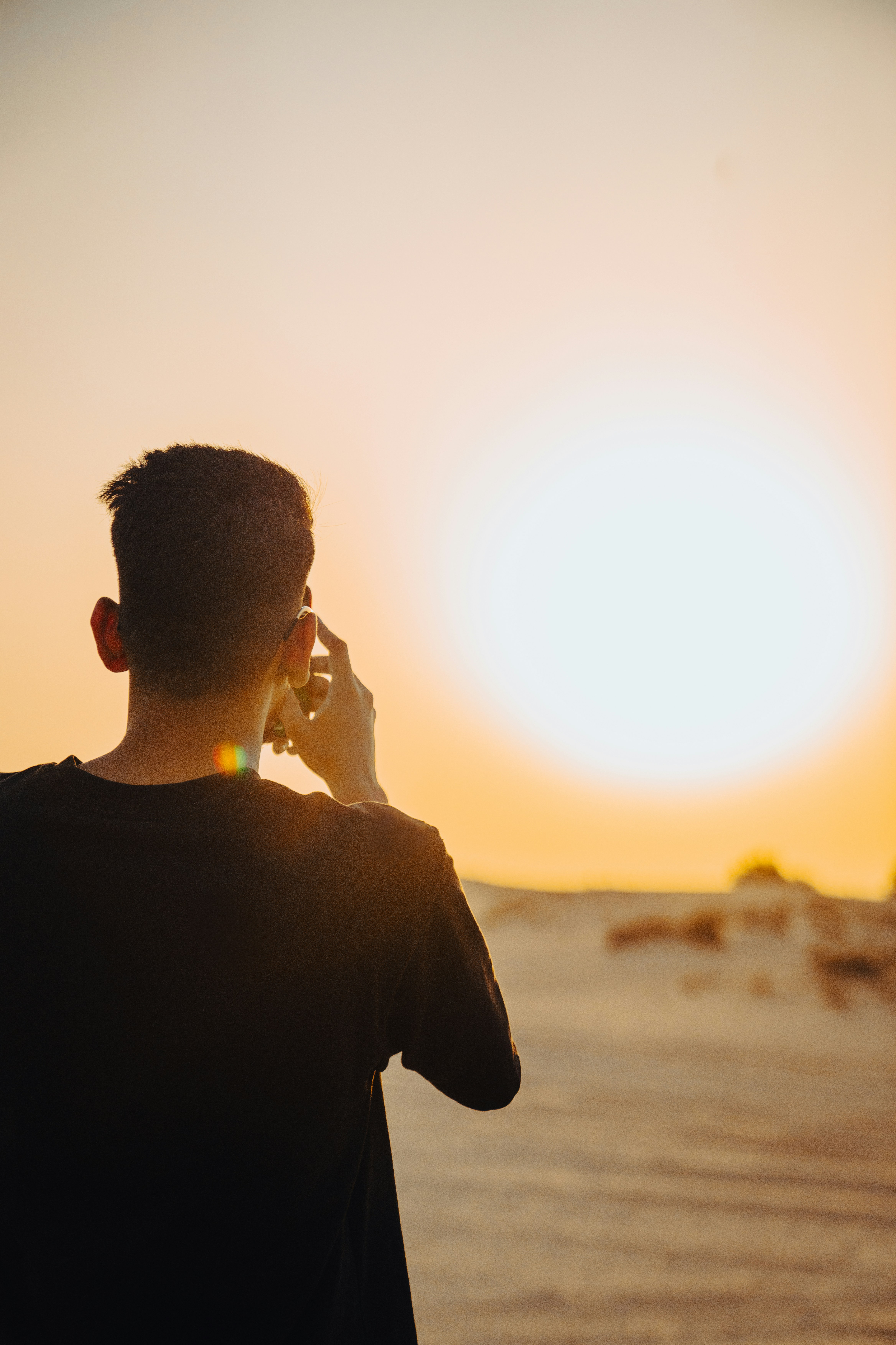 Man on phone watches a bright desert sunset