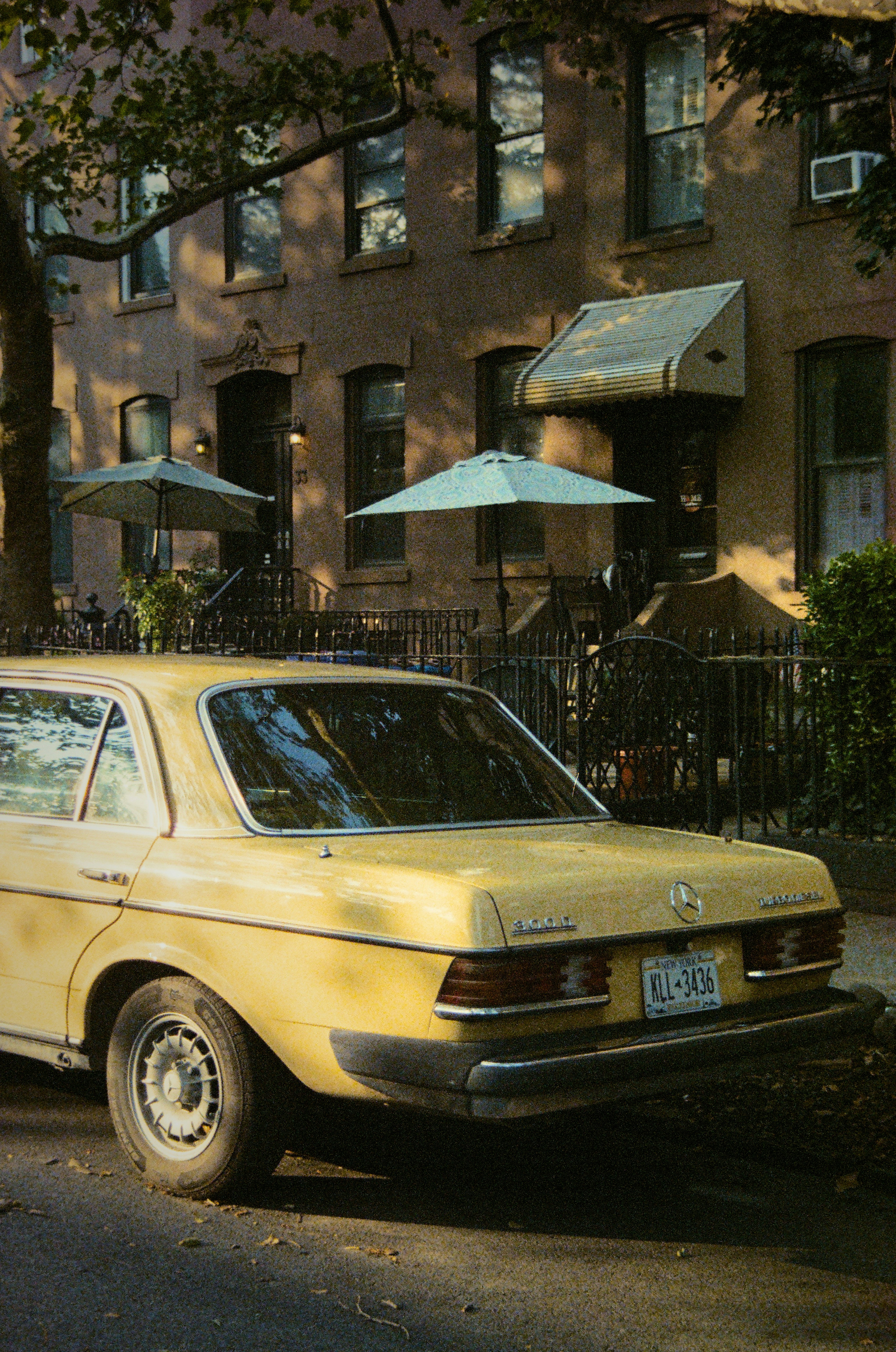 Yellow vintage car parked outside brown apartment building.