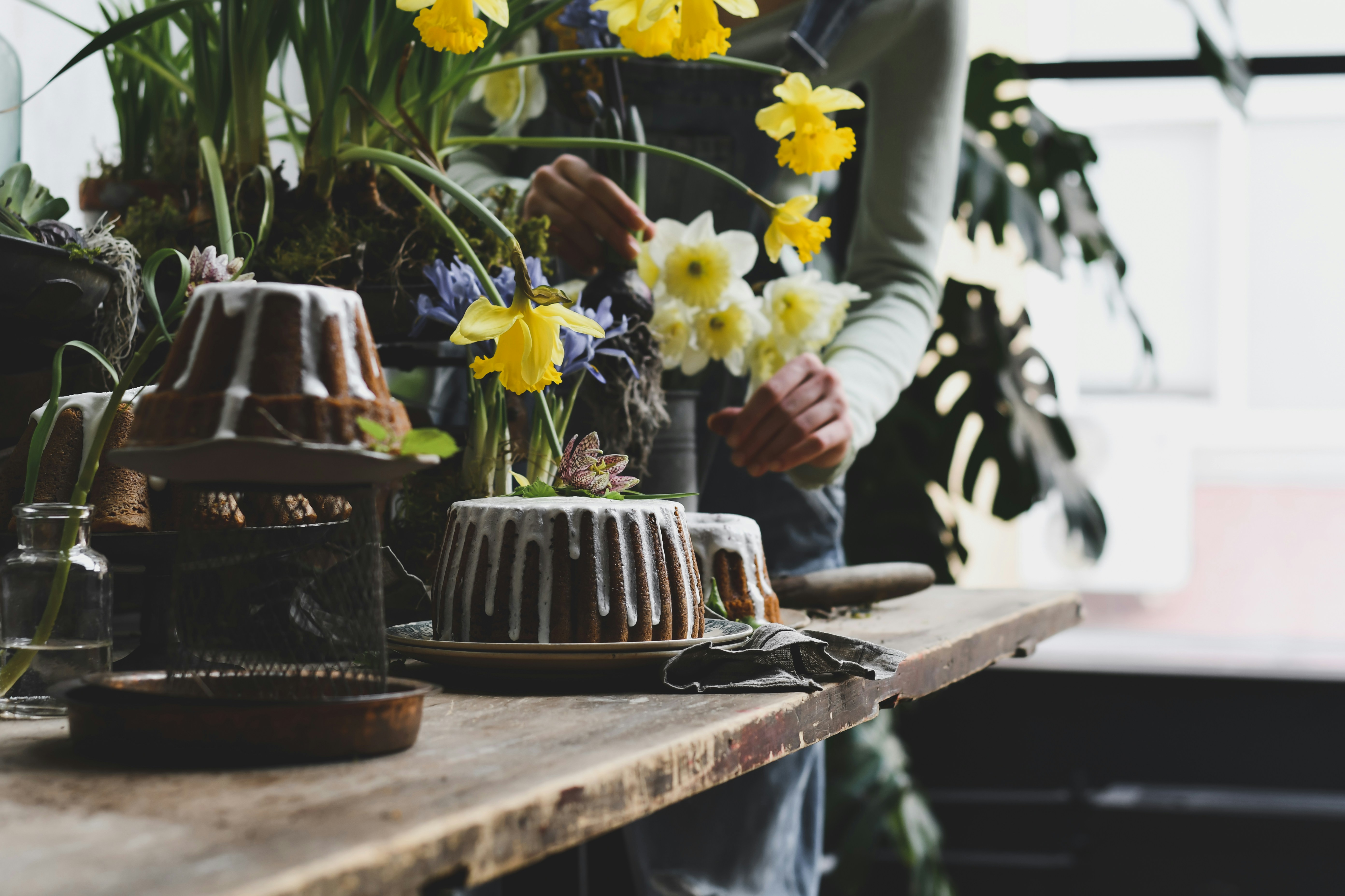 Person arranging yellow daffodils near bundt cakes.