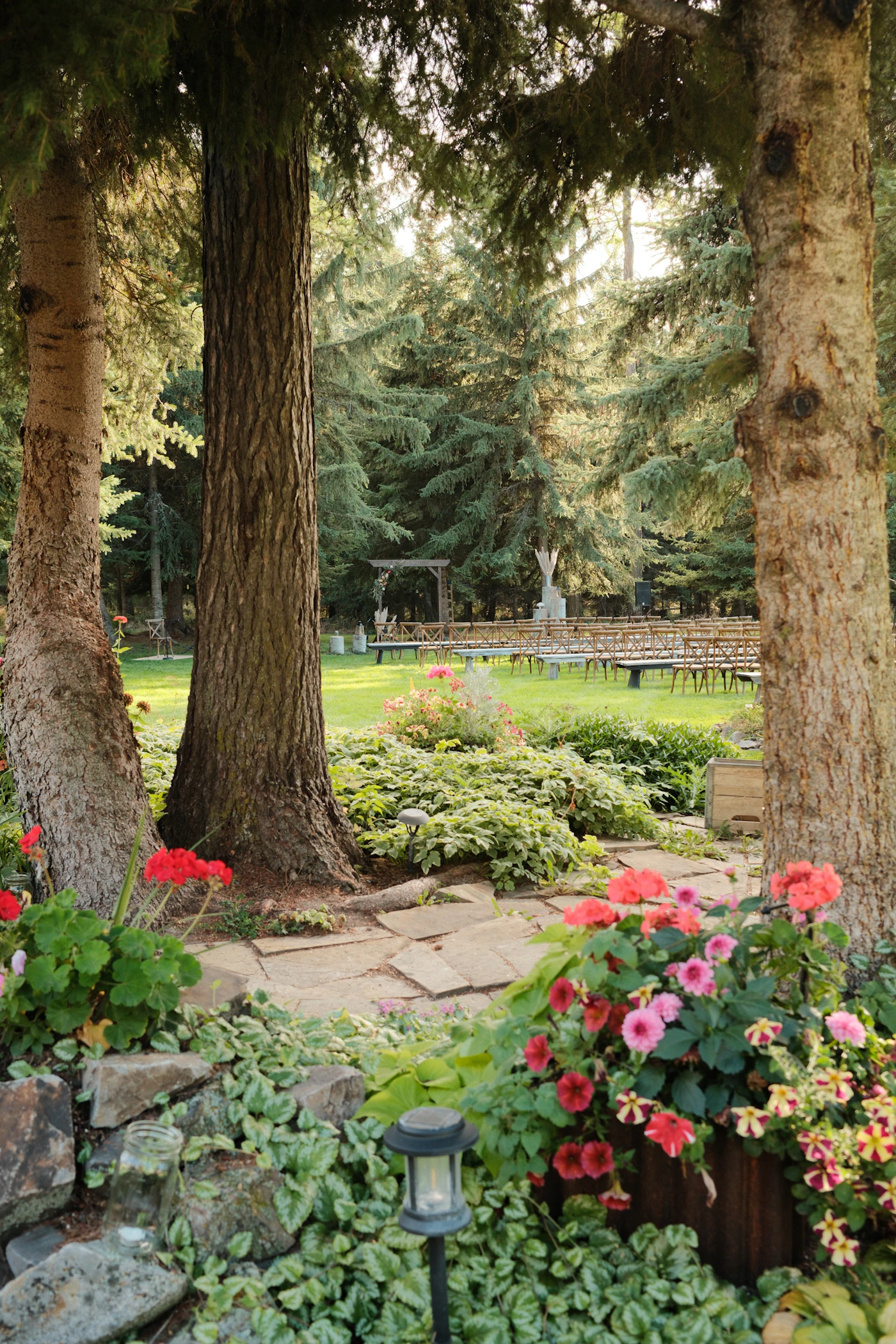 Outdoor wedding ceremony setup with wooden chairs arranged on a garden lawn surrounded by mature trees and summer flowers in full bloom