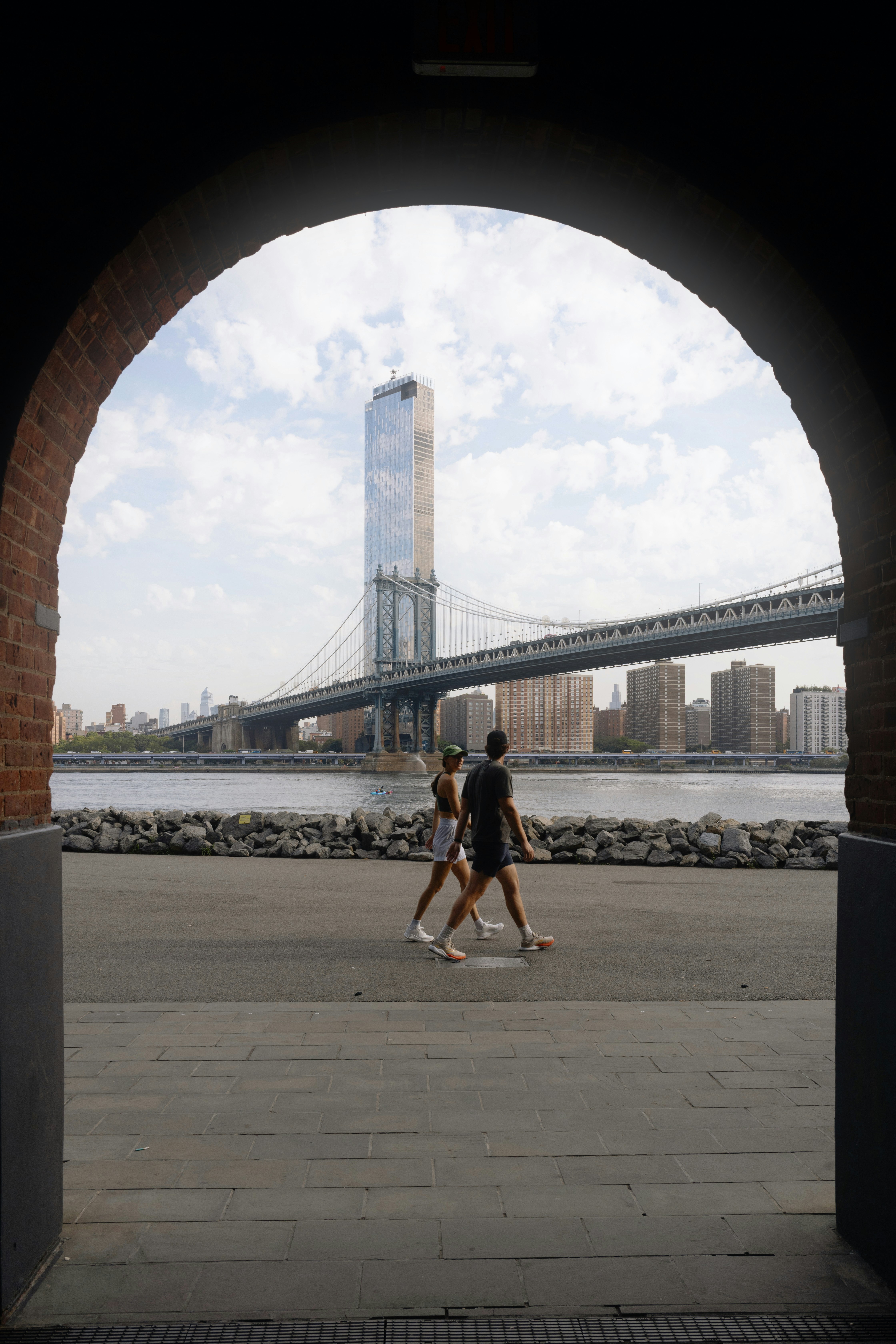 Two people walk past manhattan bridge and cityscape