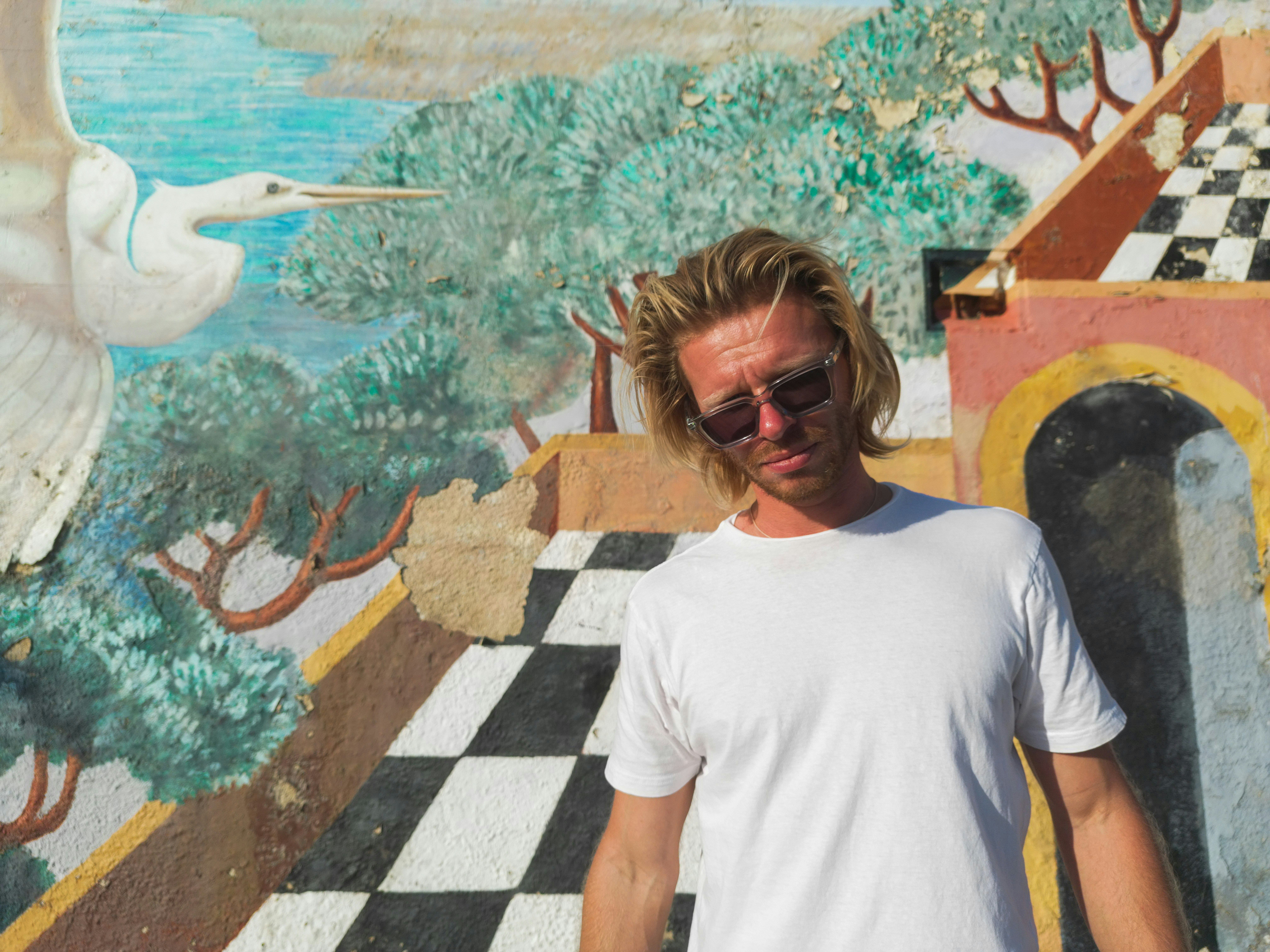 Man in white t-shirt stands before colorful mural