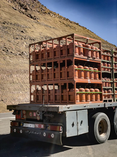 Truck carrying many orange gas cylinders on a road.