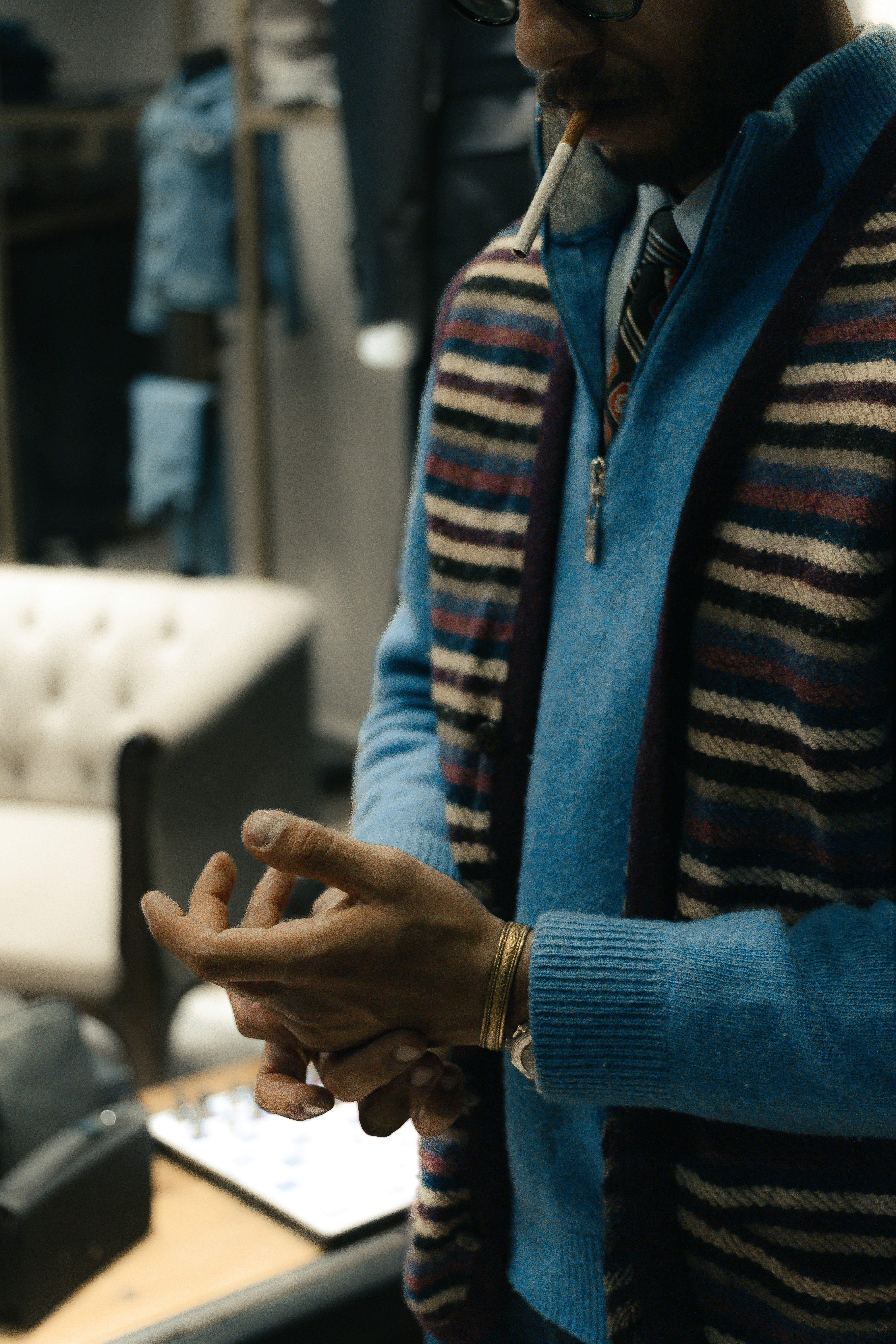 Man in blue sweater and striped scarf smoking cigarette.