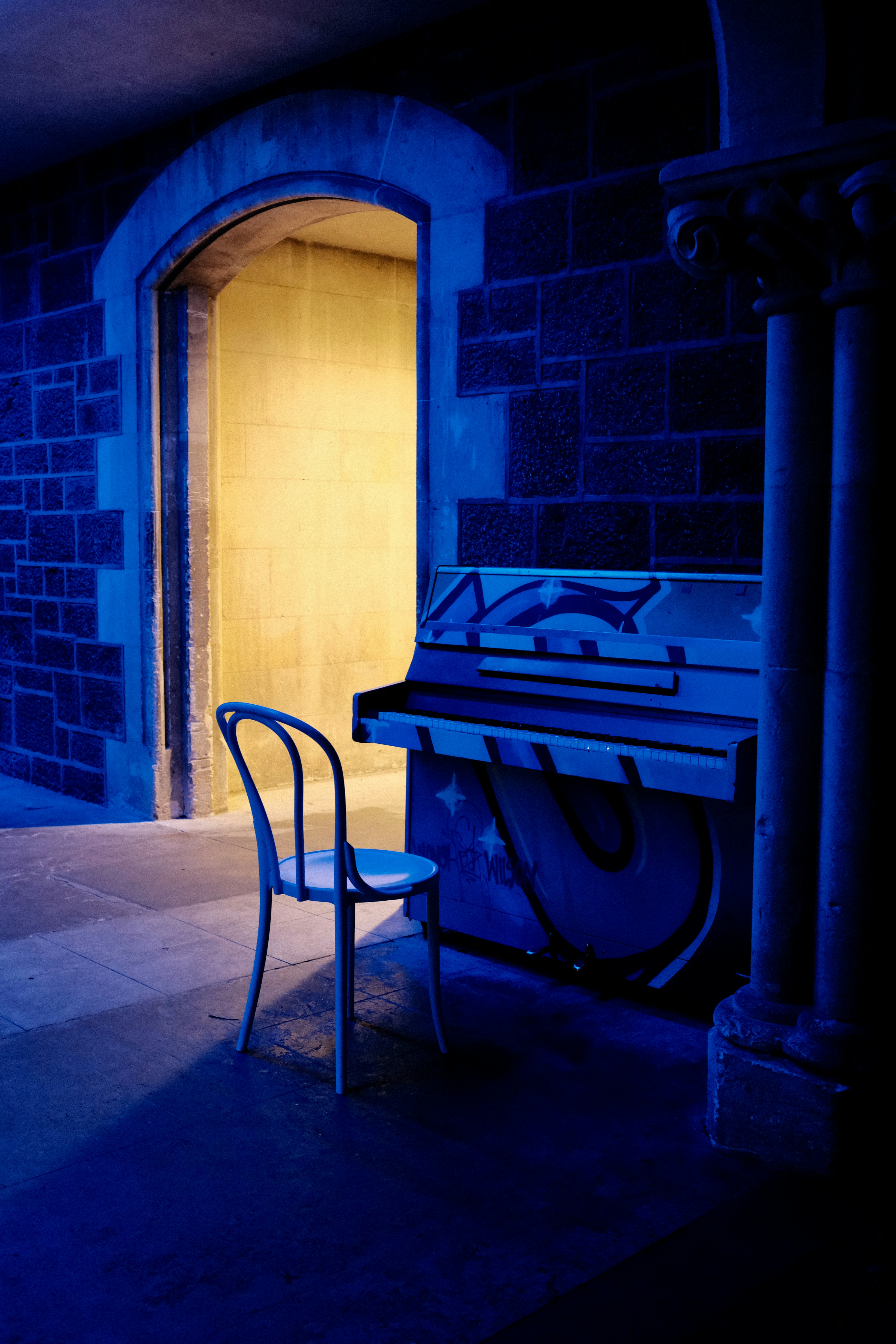 椅子とピアノが置かれた青く照らされた部屋。