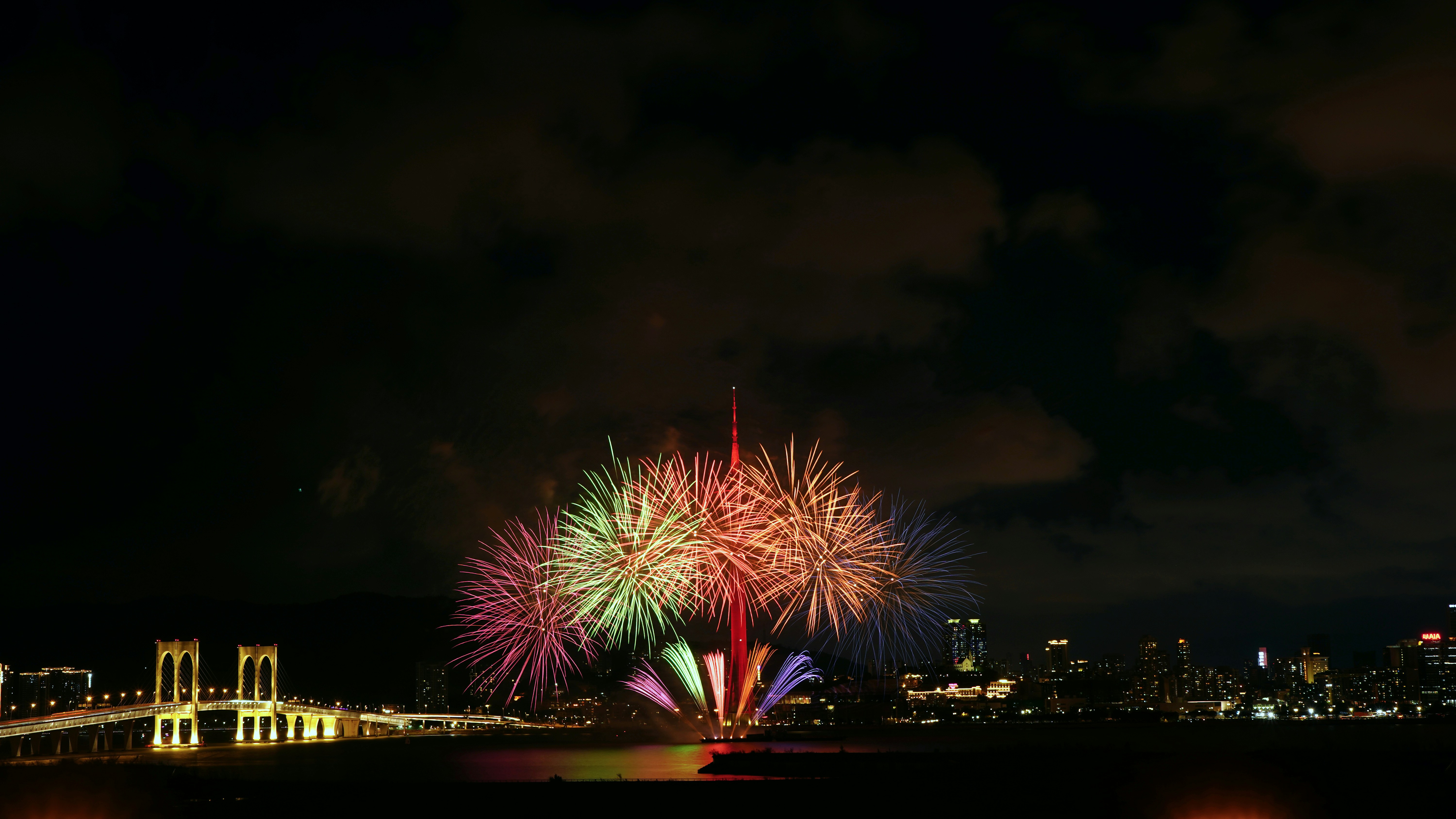 Colorful fireworks explode over a city skyline at night.