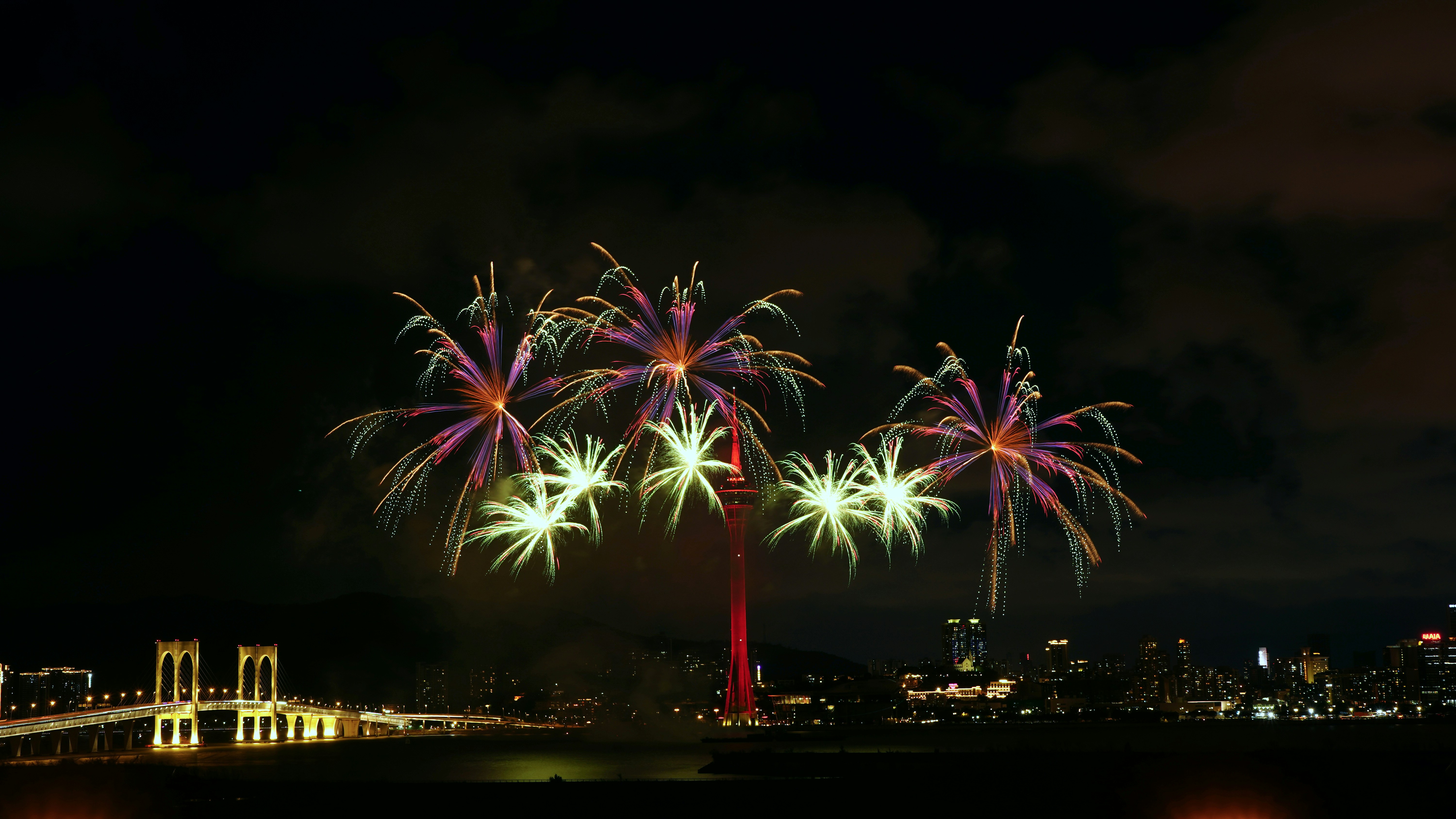 Fireworks explode over a city skyline and bridge.