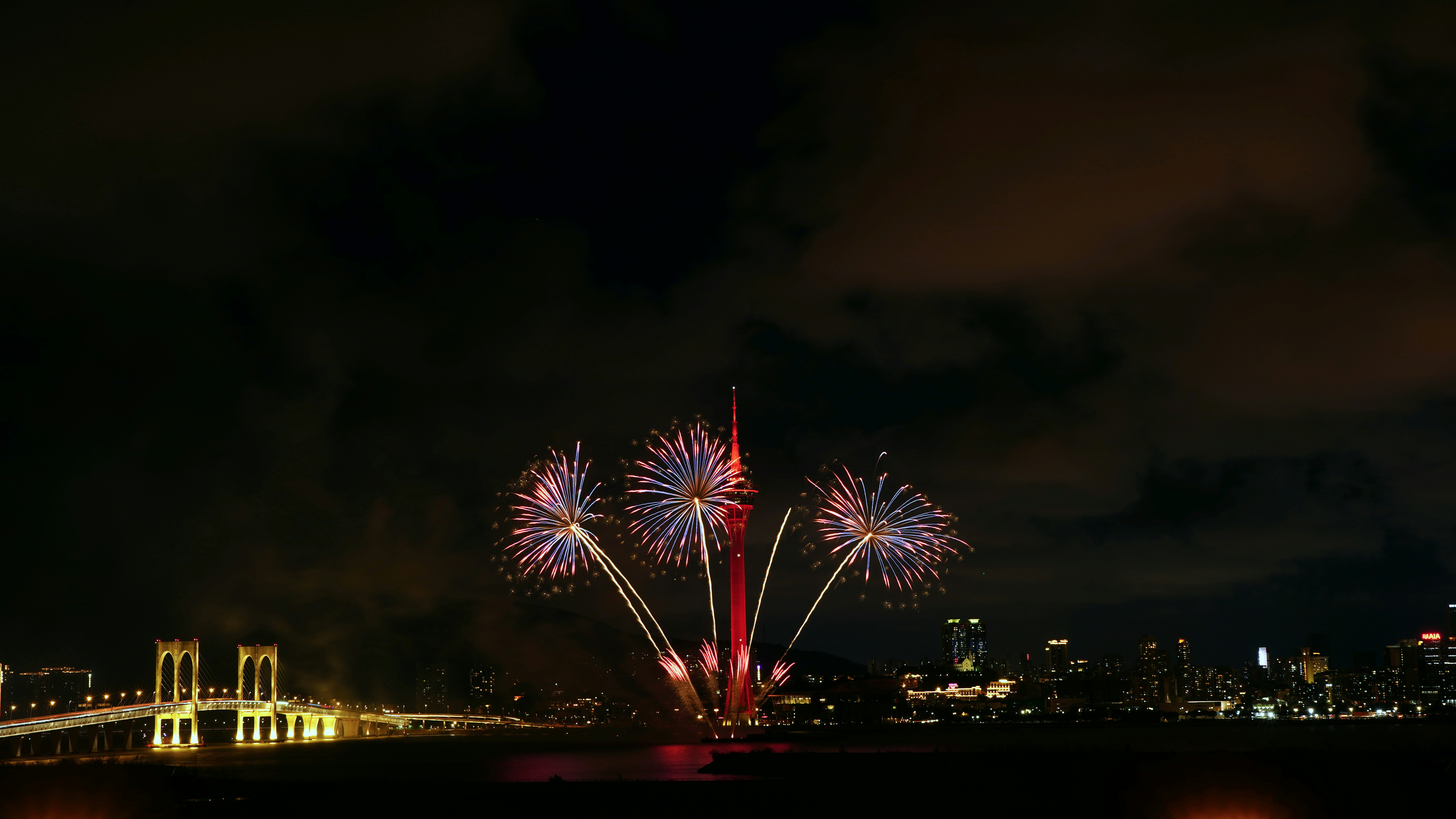 Fireworks illuminate the night sky over a city skyline.
