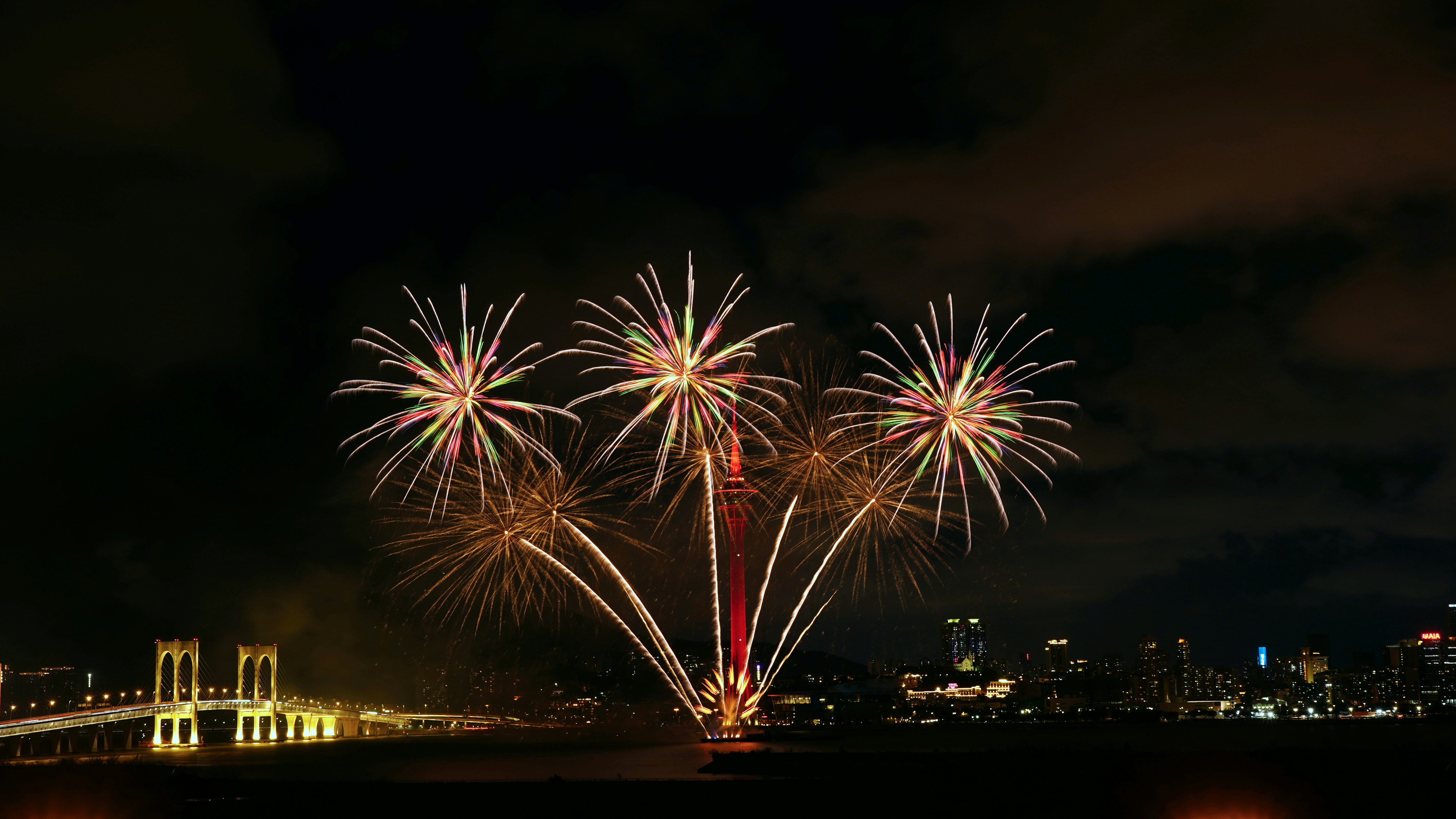 Des feux d’artifice illuminent le ciel nocturne au-dessus de l’horizon d’une ville.