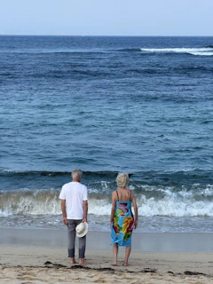 Elderly couple standing on beach watching waves