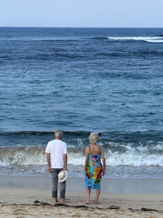 Elderly couple standing on beach watching waves
