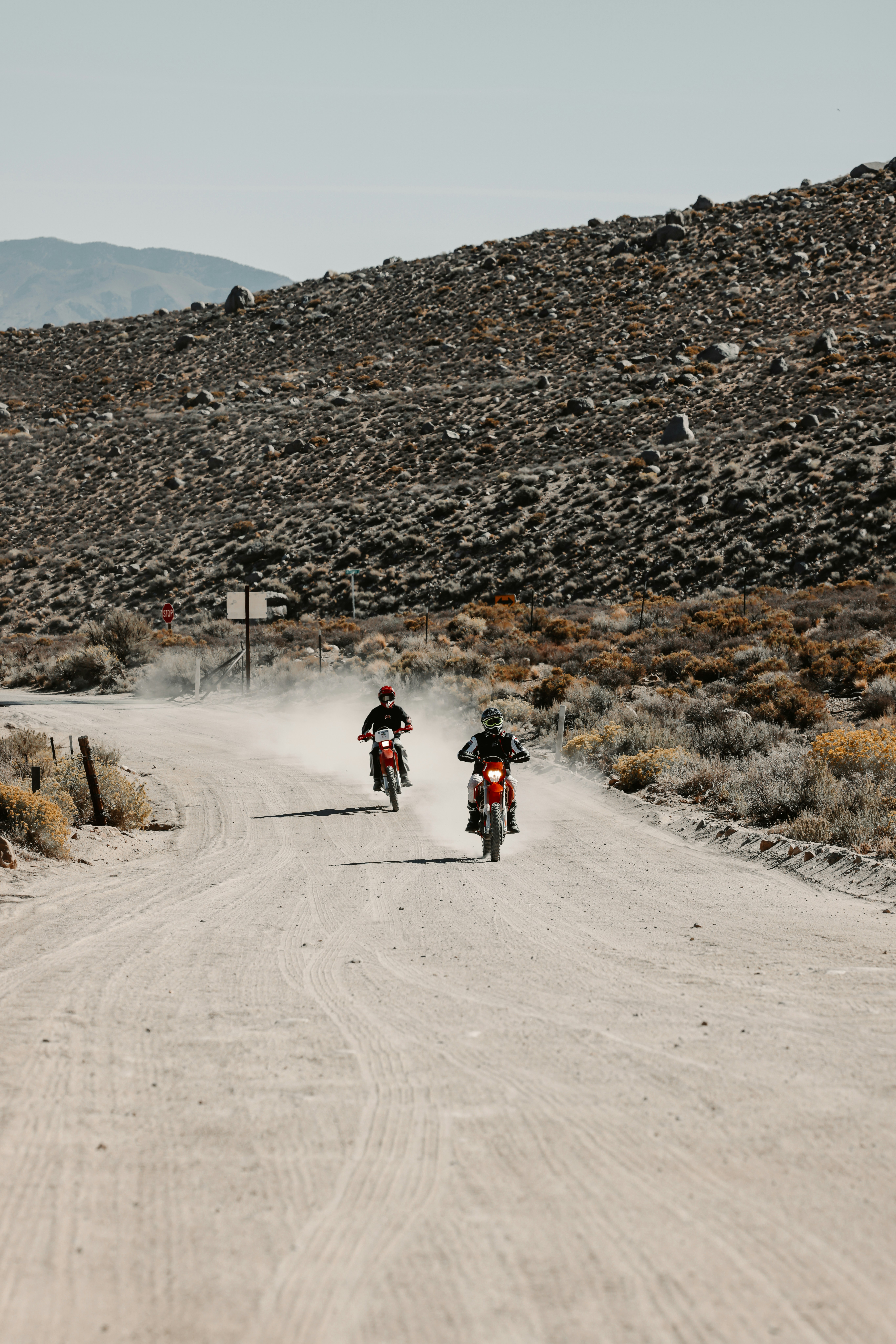 Two motorcyclists ride down a dusty desert road.